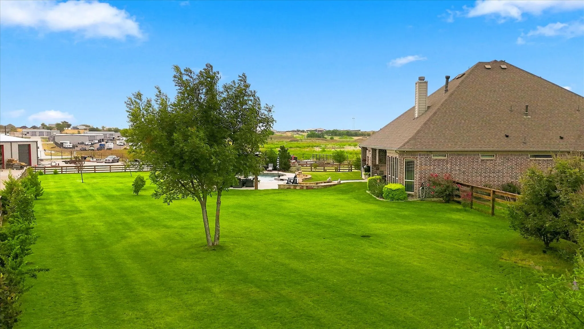 Expansive green lawn with mature trees, brick exterior, and a visible pool area