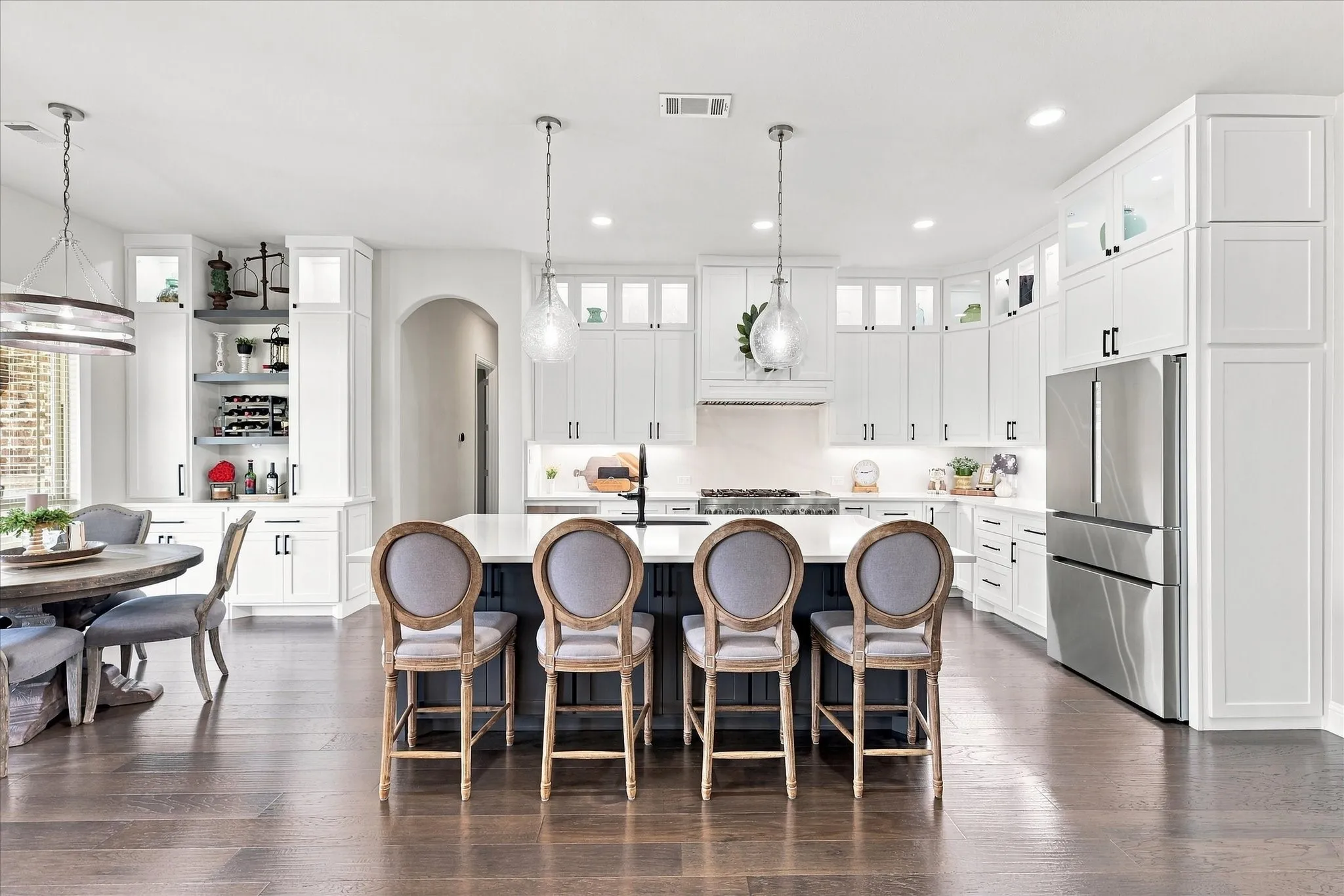 Spacious recently renovated kitchen featuring an expansive center island, white cabinetry, dark wood-finish flooring, stainless steel appliances, and a built-in beverage bar with open shelving