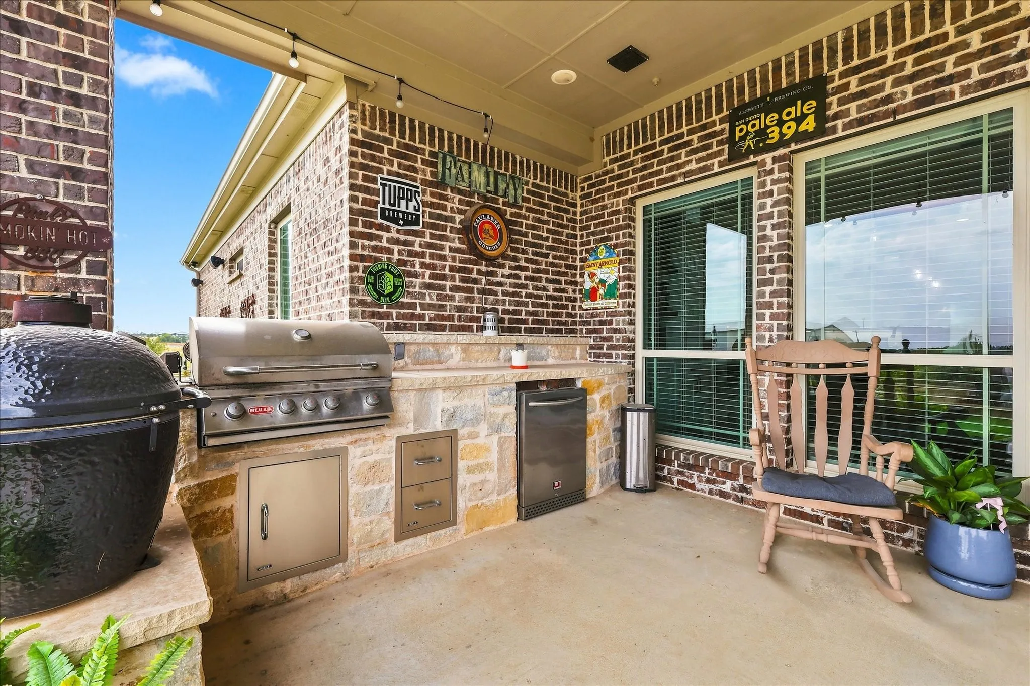 Covered outdoor patio featuring brick and stone-veneer walls, a built-in grill, and string lighting