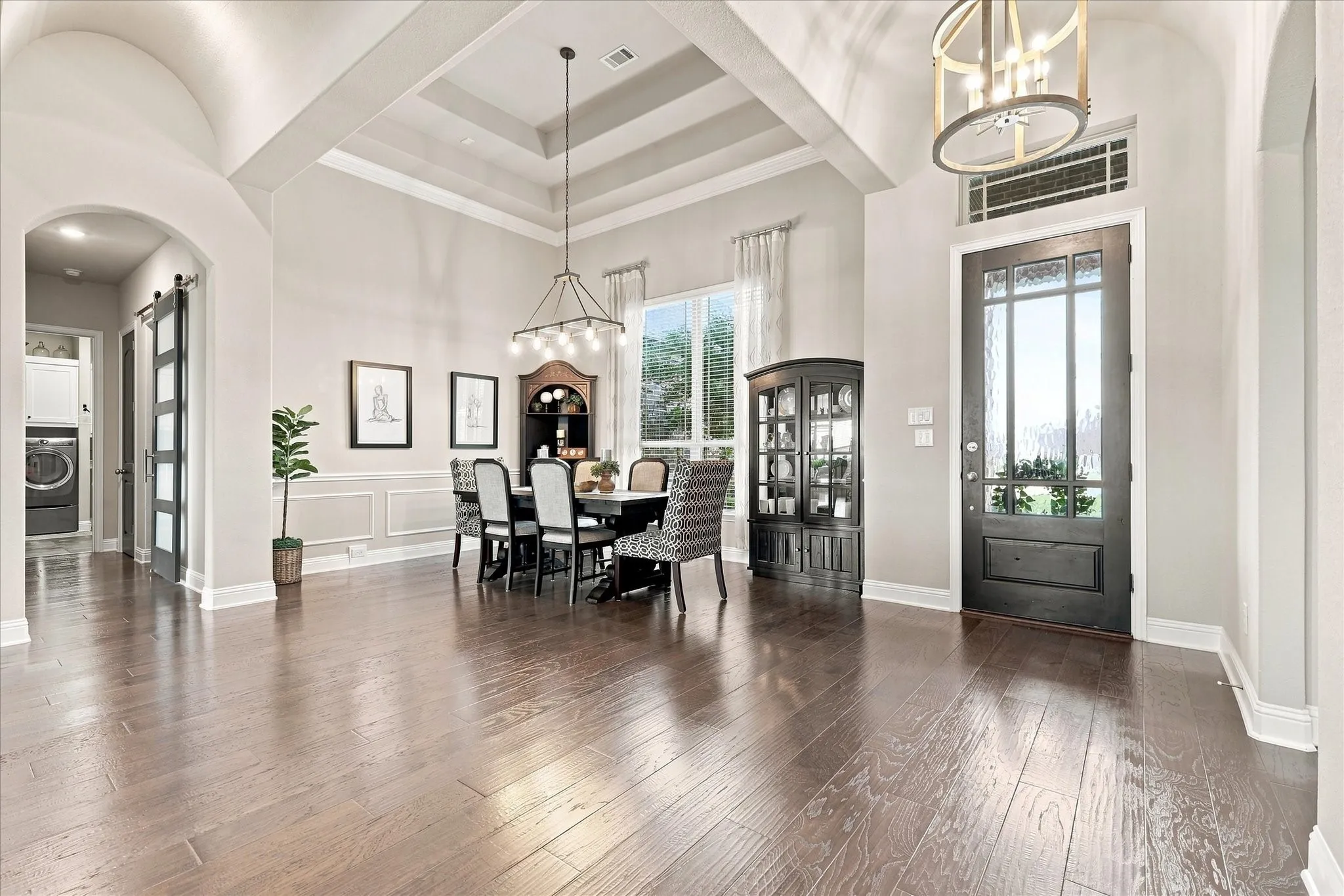 Wood-finish flooring throughout, tray ceiling with chandelier, arched entryway, wainscoting, and a full-light entry door