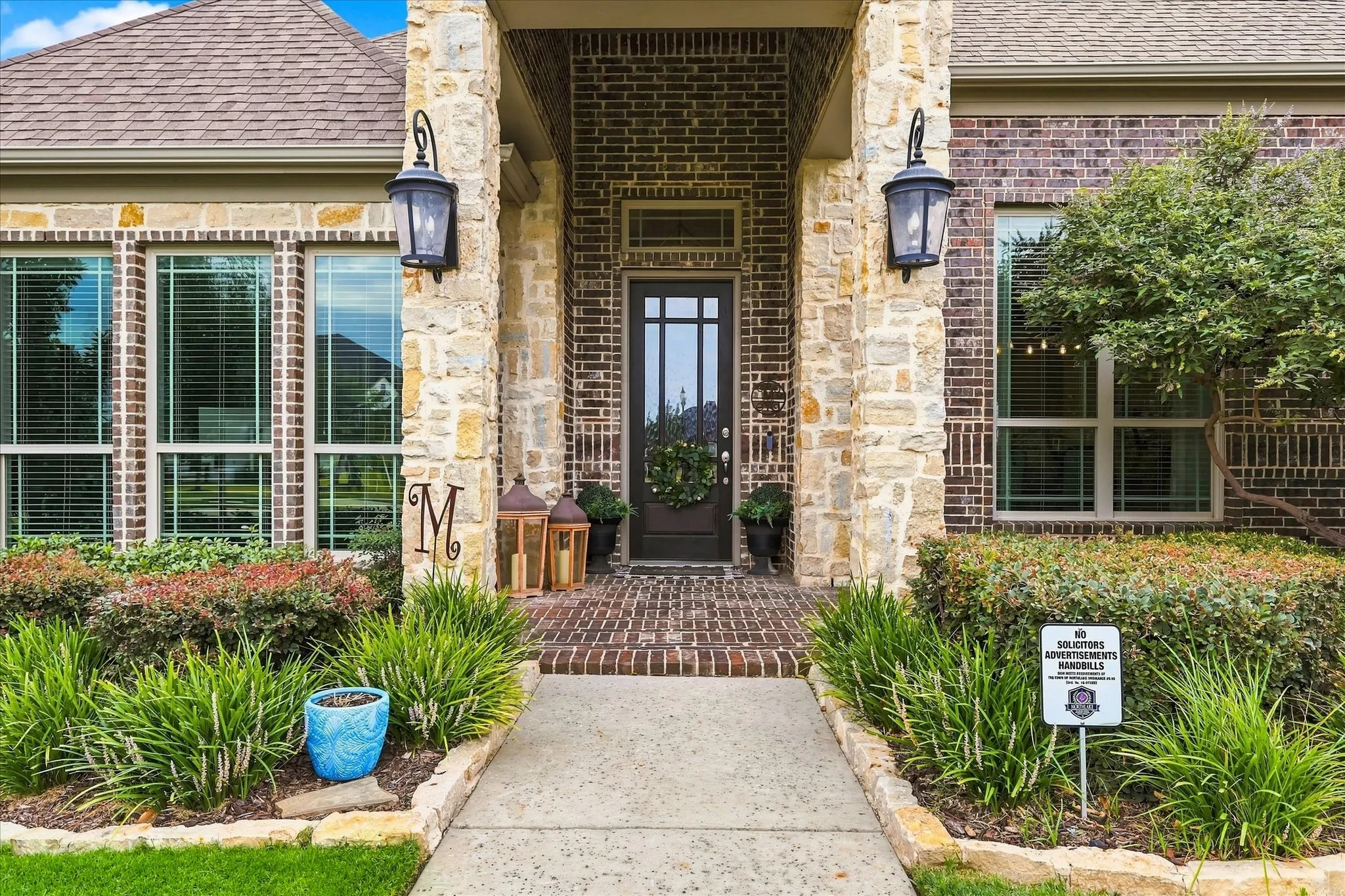 Brick and stone facade with a dark wood front door, covered entry, and sconce lighting
