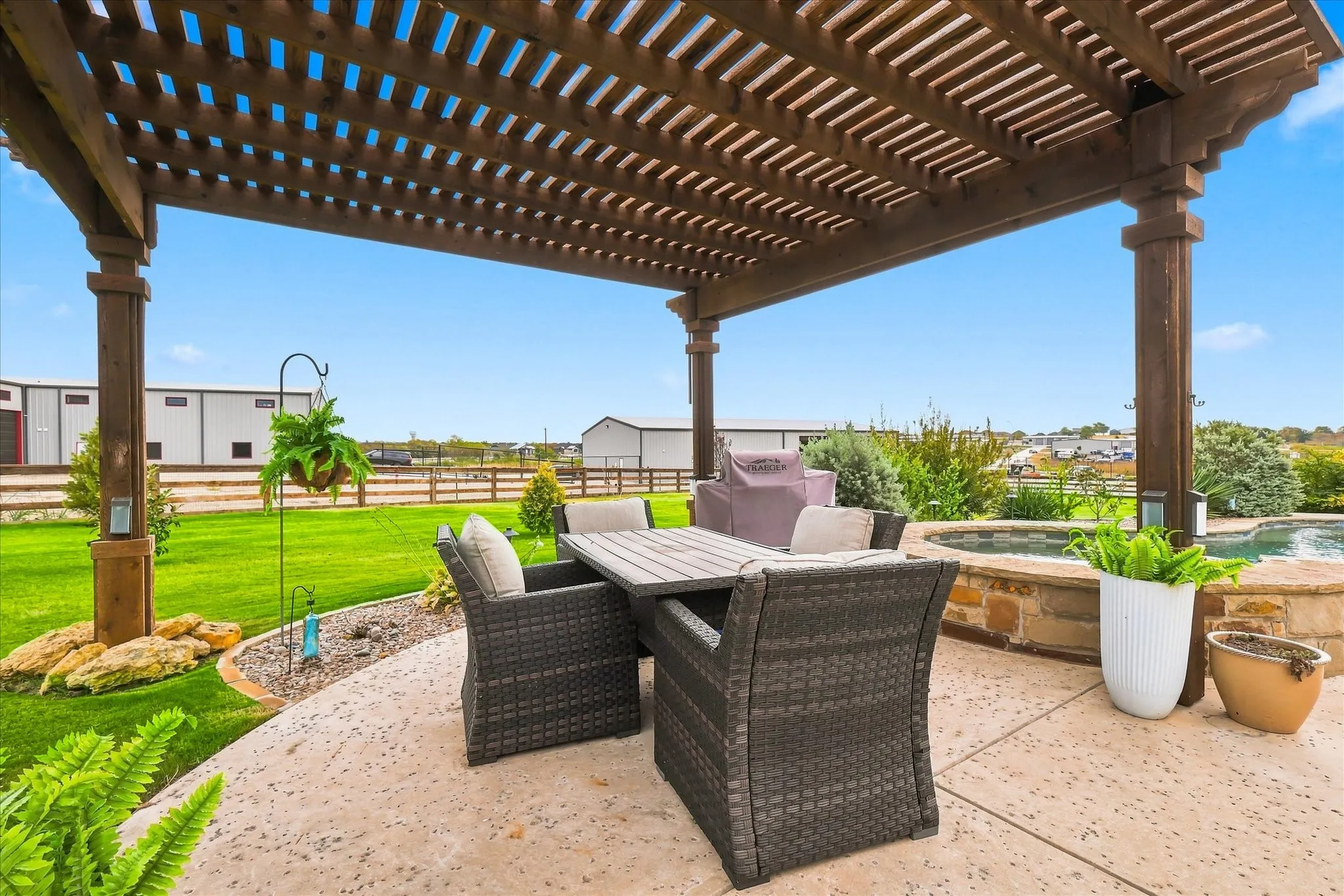 Expansive outdoor living area featuring a wooden pergola, concrete patio, stone-clad spa, and manicured lawn