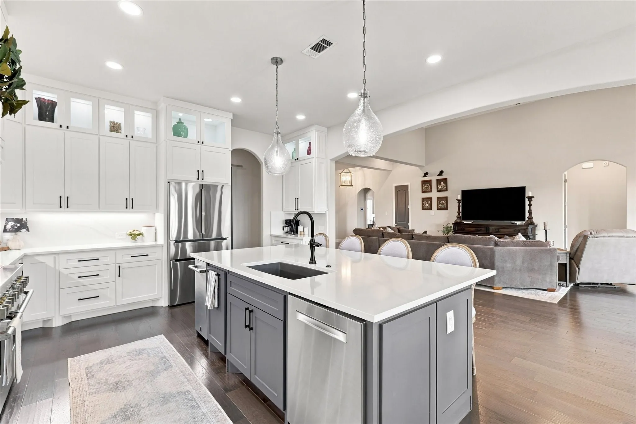 Open-concept kitchen with white cabinetry and a gray island featuring a built-in sink and stainless steel appliances, dark wood-finish flooring, and recessed lighting