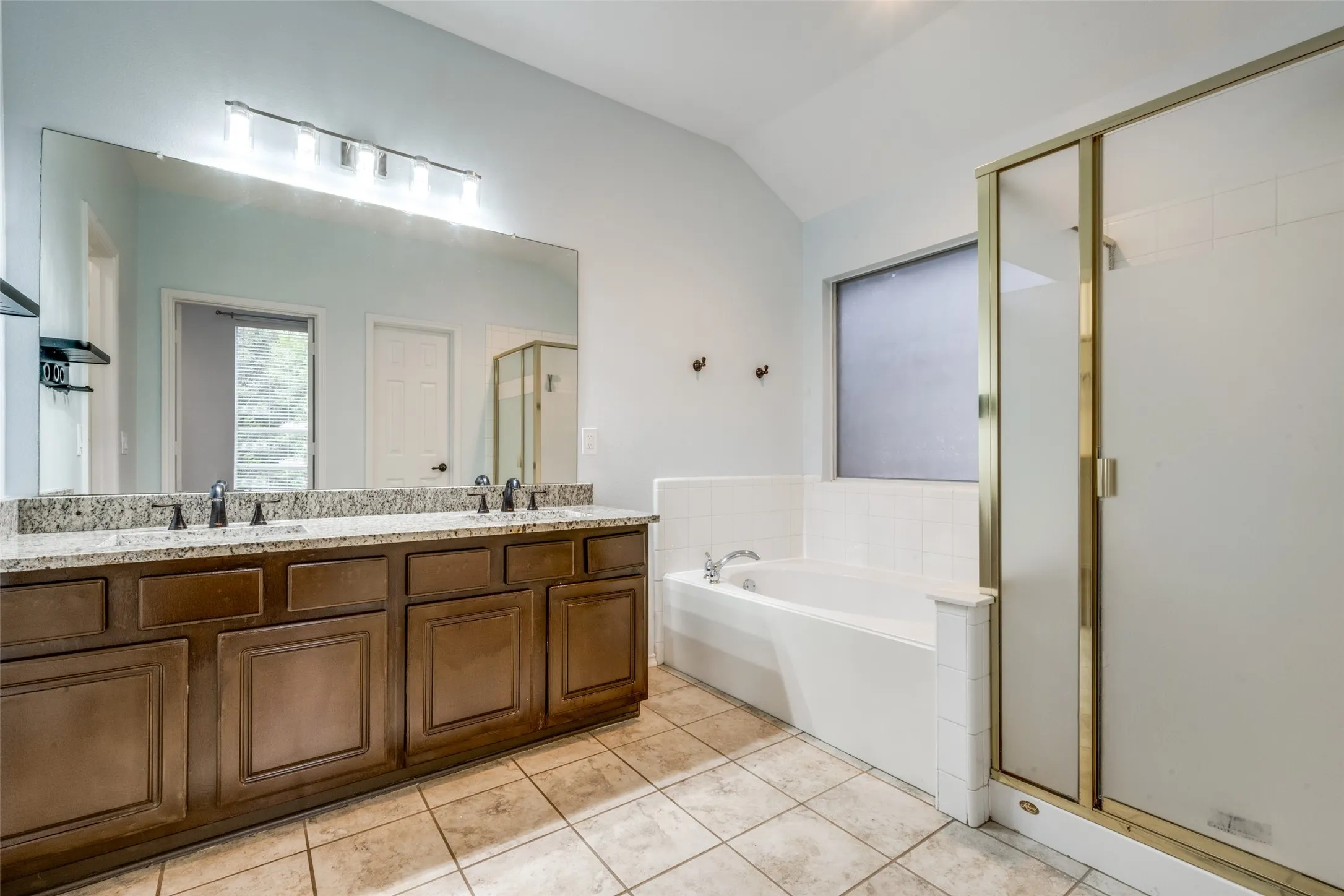 Dual vanity with granite-style countertop, large frameless mirror, separate soaking tub, and tile-surround shower with framed glass enclosure