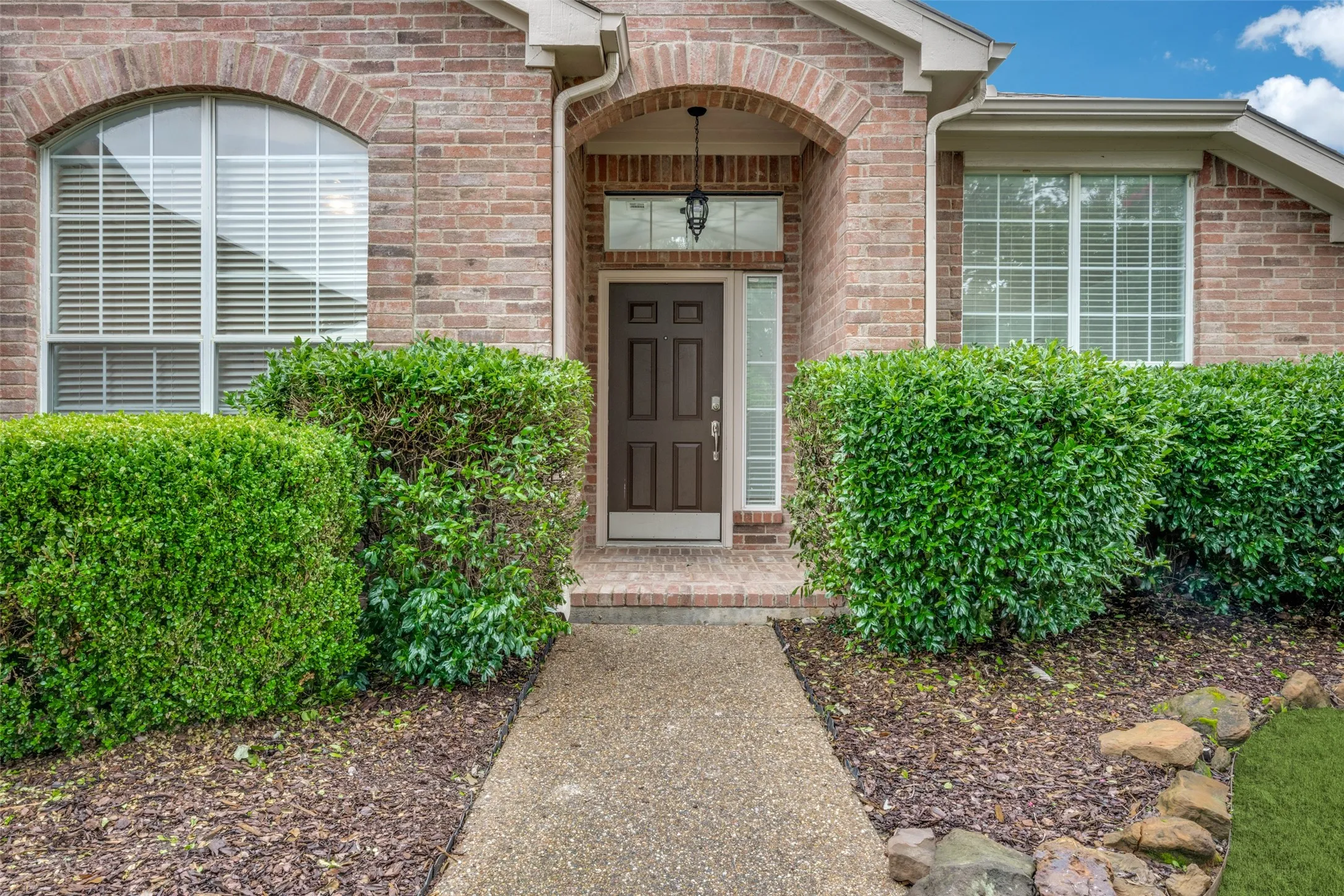 Brick facade with arched window details, covered entry, and mature landscaping