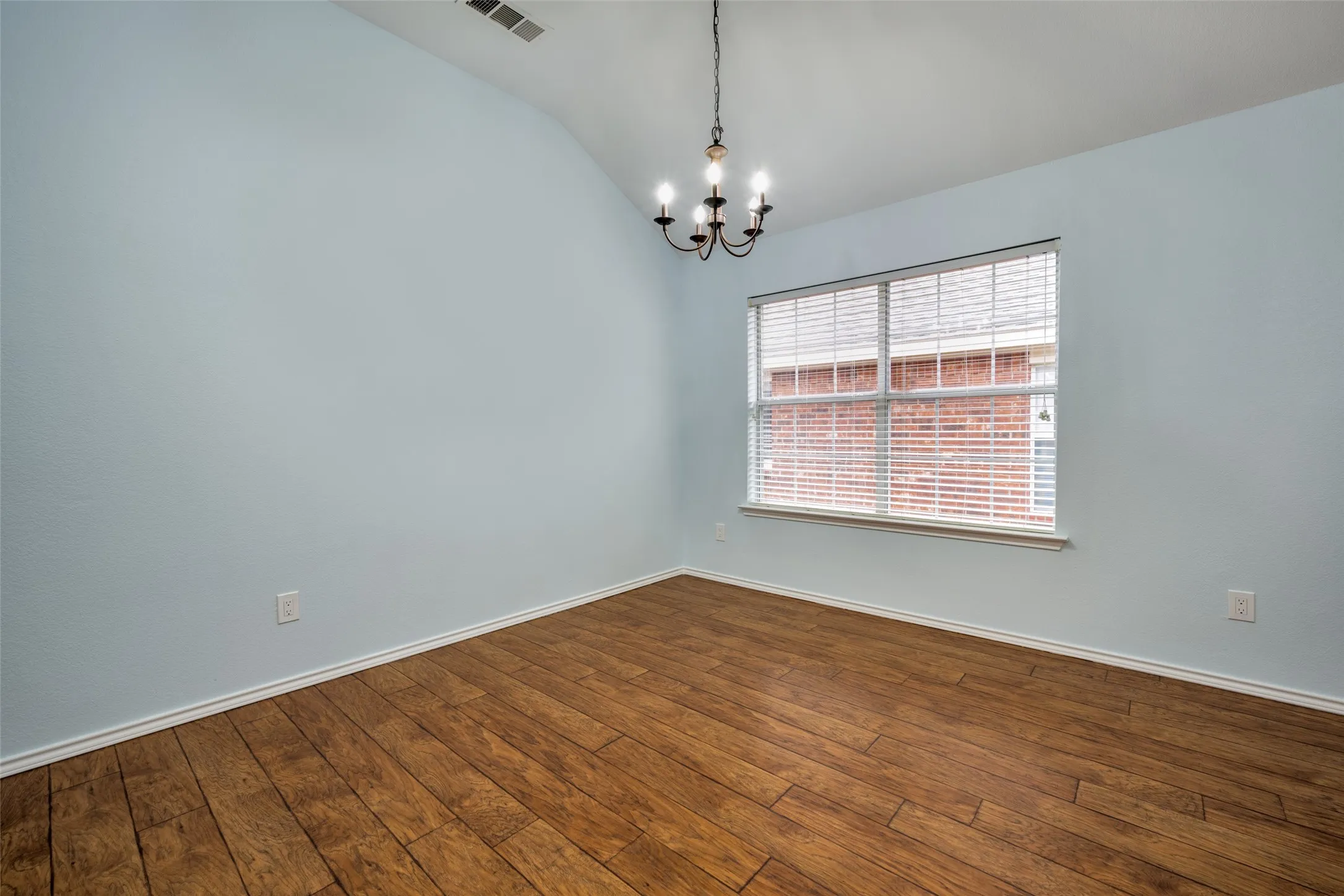 Vaulted ceiling with a chandelier, wood-finish flooring, and a window with blinds