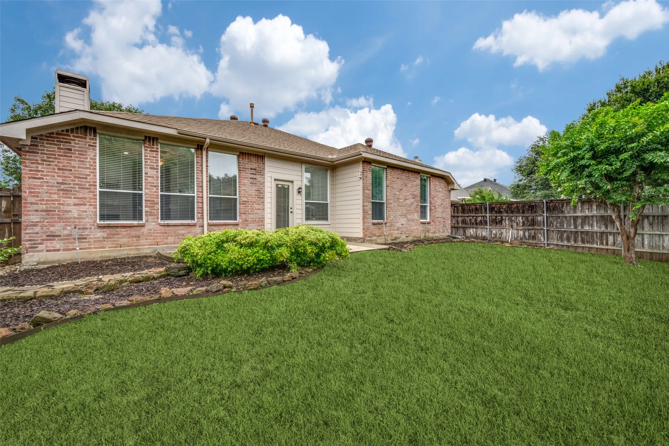 Expansive backyard featuring a manicured lawn, brick exterior, and a privacy fence