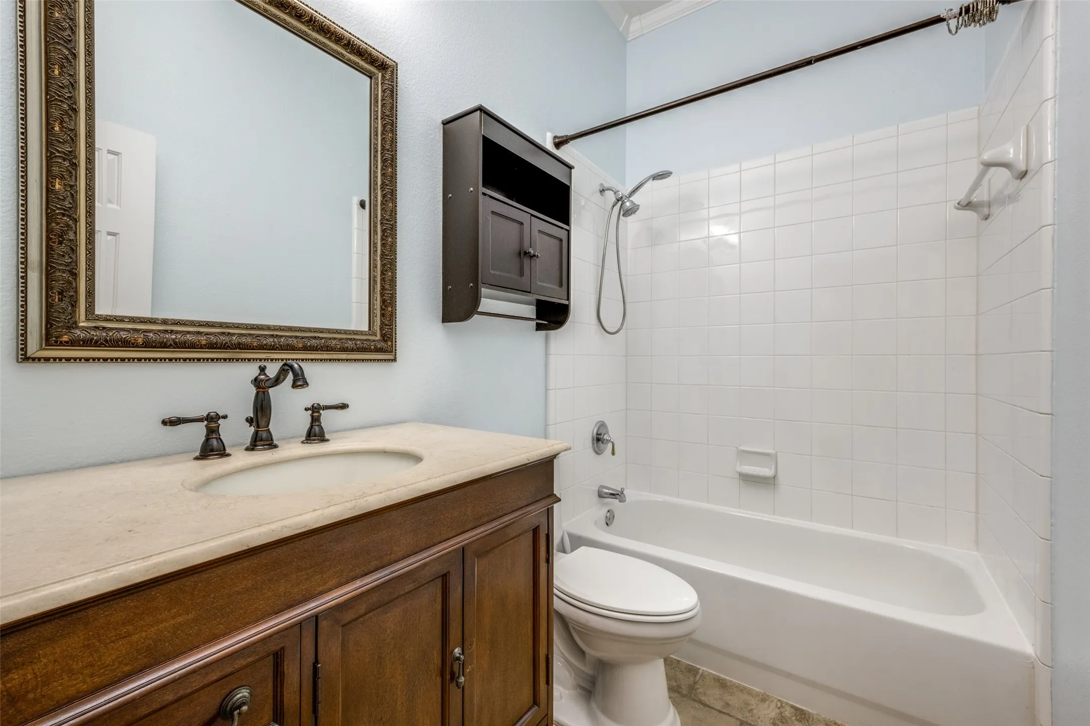 Vanity with integrated sink and dark bronze faucet, framed mirror, built-in storage cabinet, white subway tile shower surround, and a white bathtub