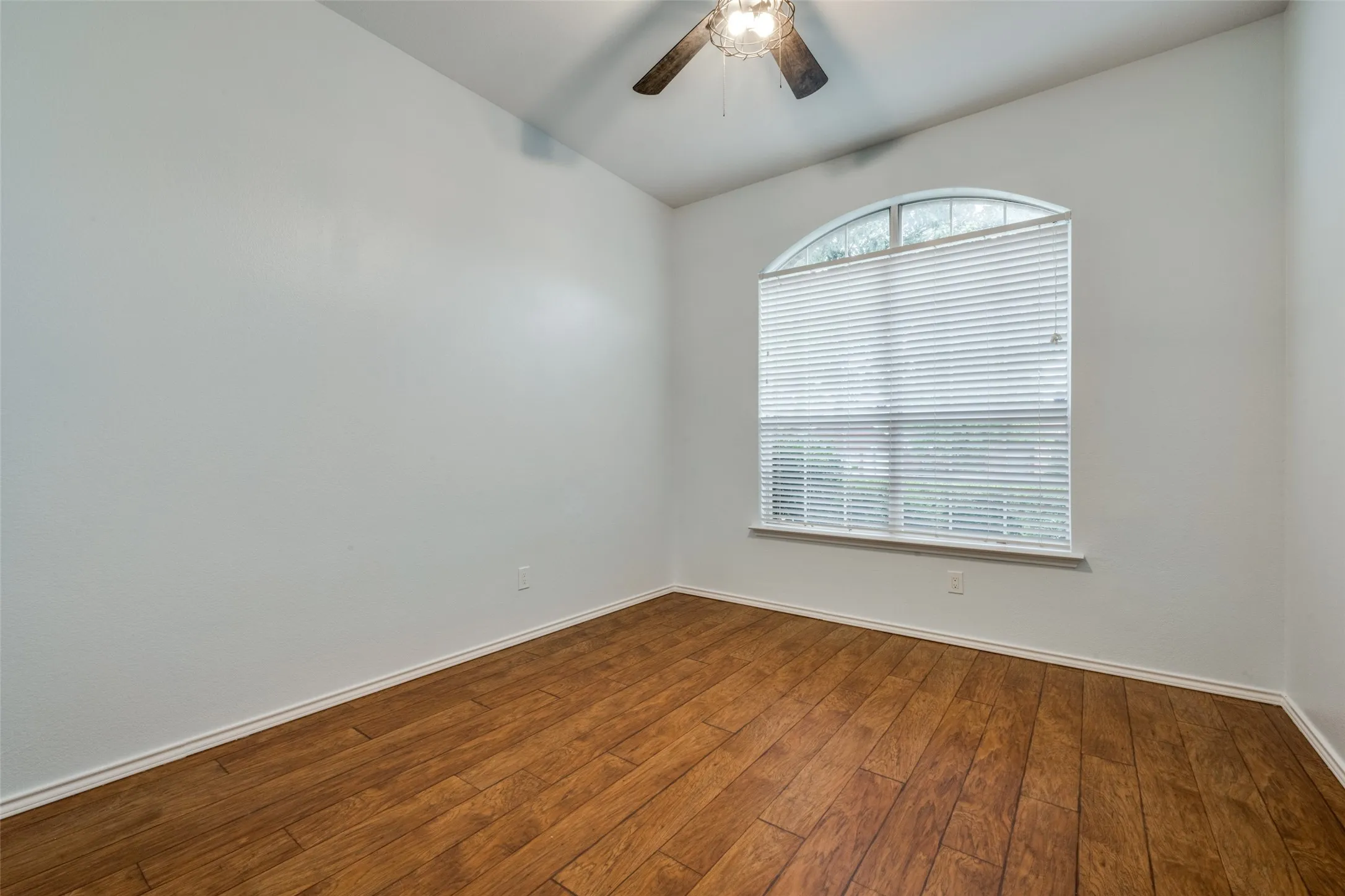 Vaulted ceiling featuring a ceiling fan, wood-finish flooring, and an arched window with blinds