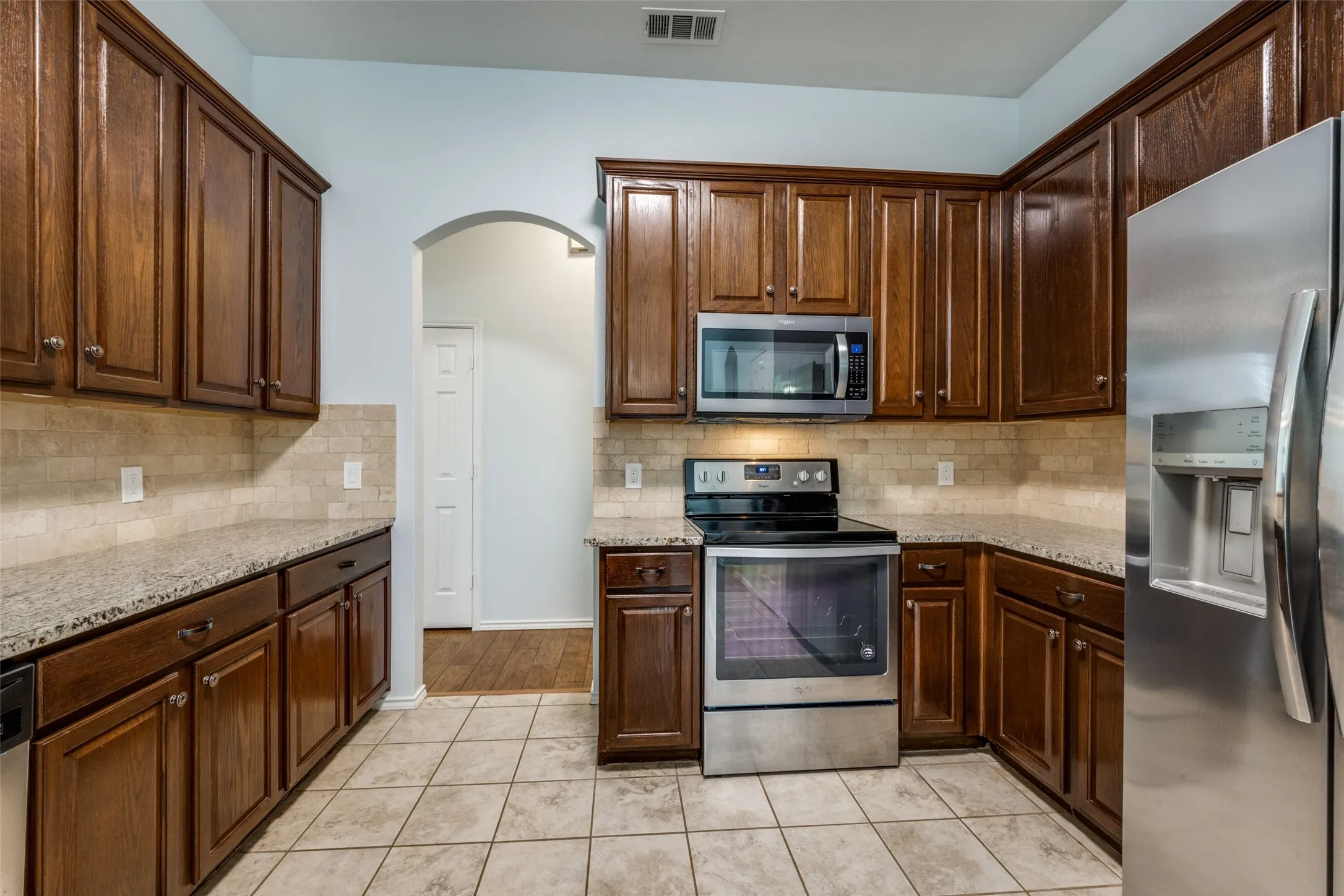 Kitchen featuring wood-finish cabinetry, granite countertops, stainless steel appliances, and a tiled backsplash