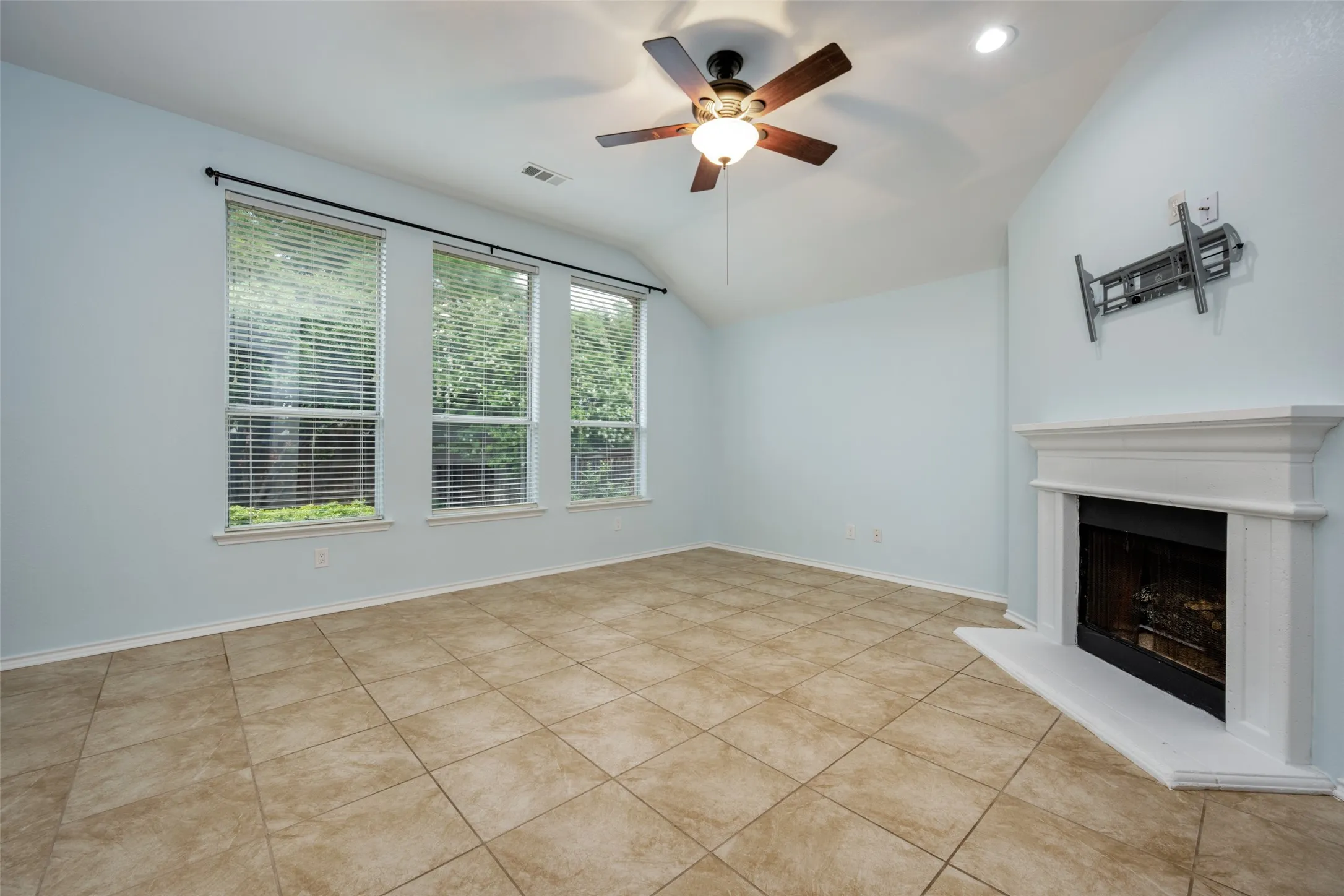 Vaulted ceiling, tiled flooring, built-in fireplace, three large windows, and a ceiling fan with integrated lighting