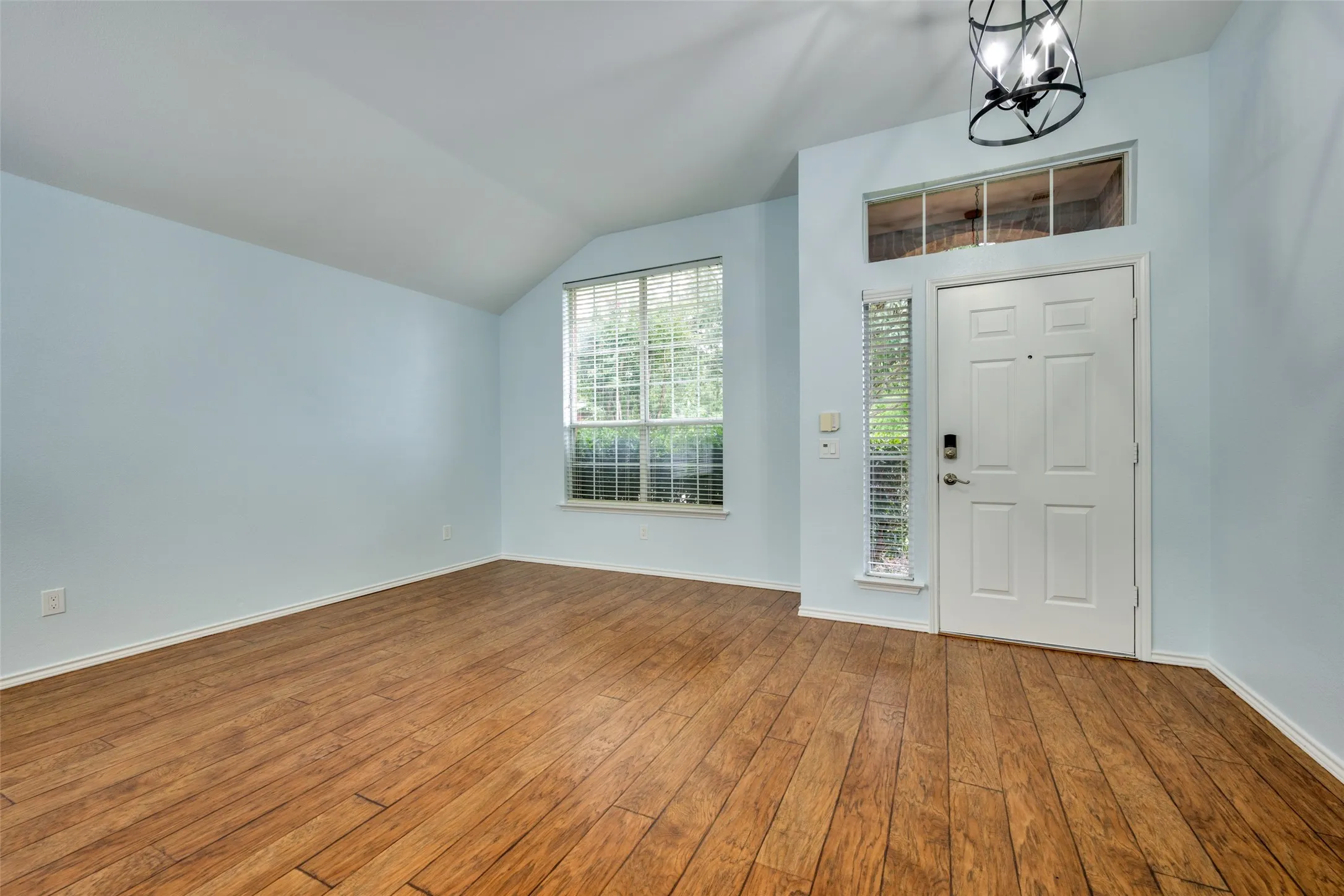 Vaulted ceiling accentuates the entry, featuring a paneled door, transom window, and a decorative ceiling light fixture