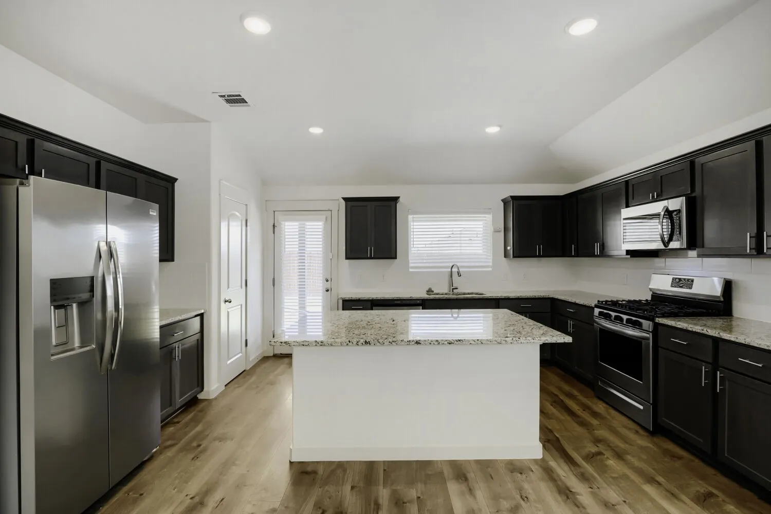 Kitchen featuring wood-finish flooring, dark cabinetry, light countertops, stainless steel appliances, and a central island