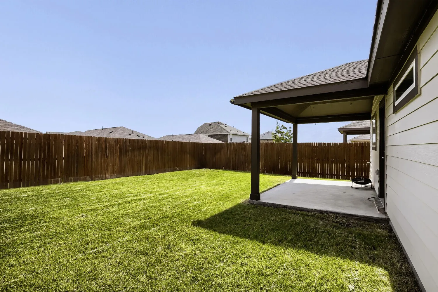 Expansive backyard featuring a manicured lawn, full wood privacy fence, and a covered patio with concrete flooring