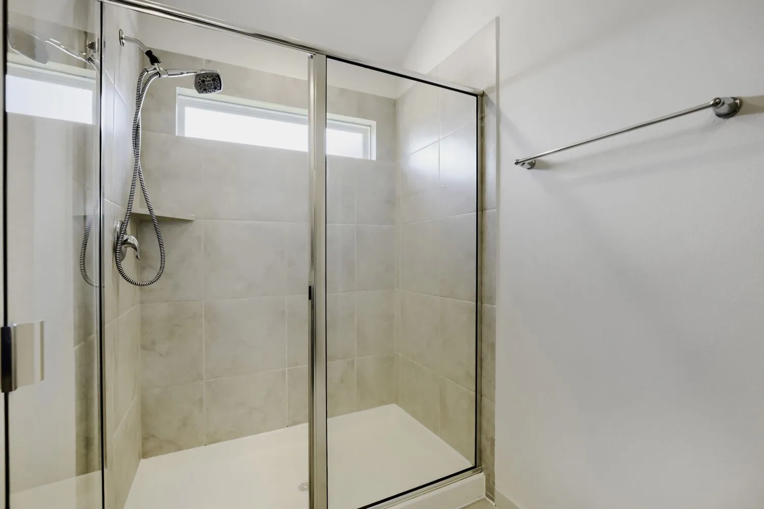 Glass-enclosed shower featuring a handheld showerhead and tiled walls