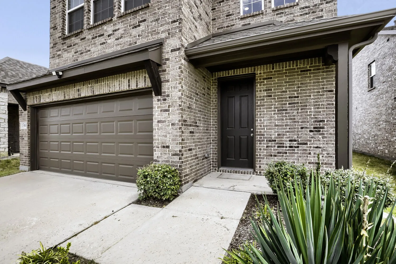 Brick exterior with a dark-paneled garage door, covered entryway, and mature landscaping