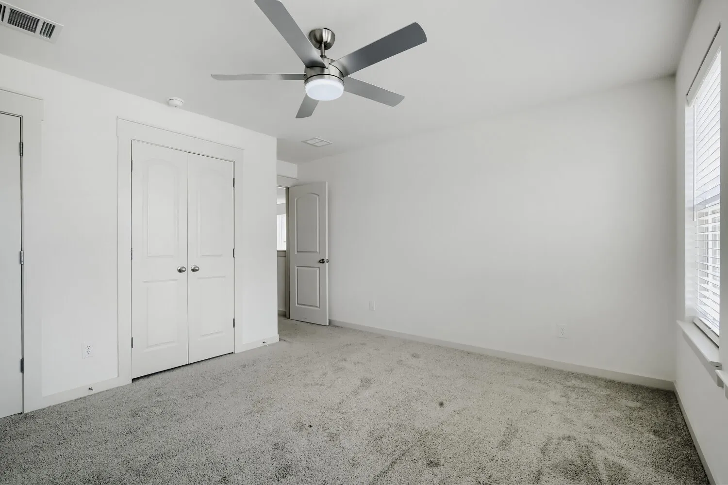 Neutral color palette, grey carpet, ceiling fan with integrated lighting, white interior doors, and window with blinds