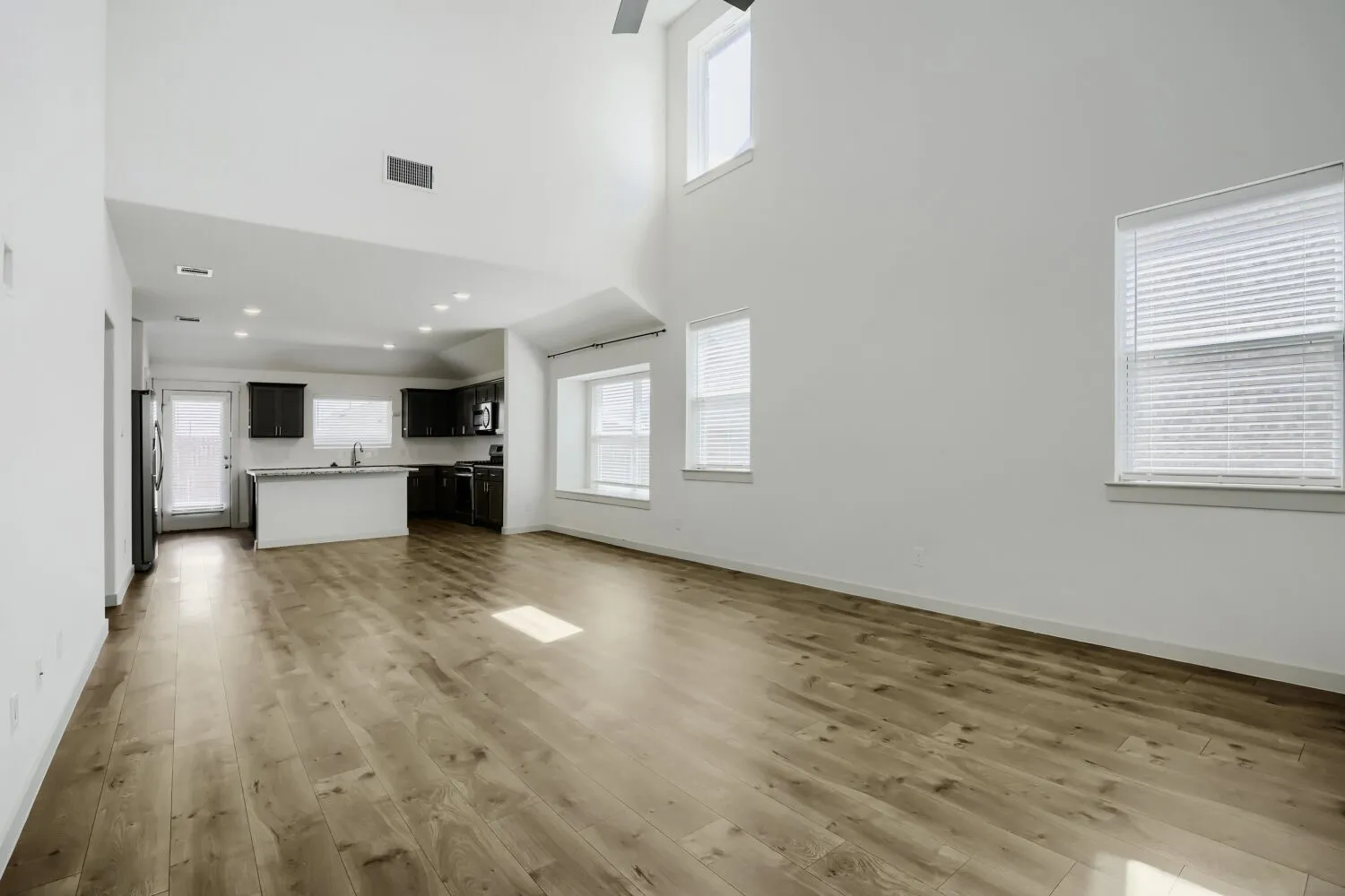 Expansive open-concept living area featuring wood-finish flooring, high vaulted ceilings, and recessed lighting