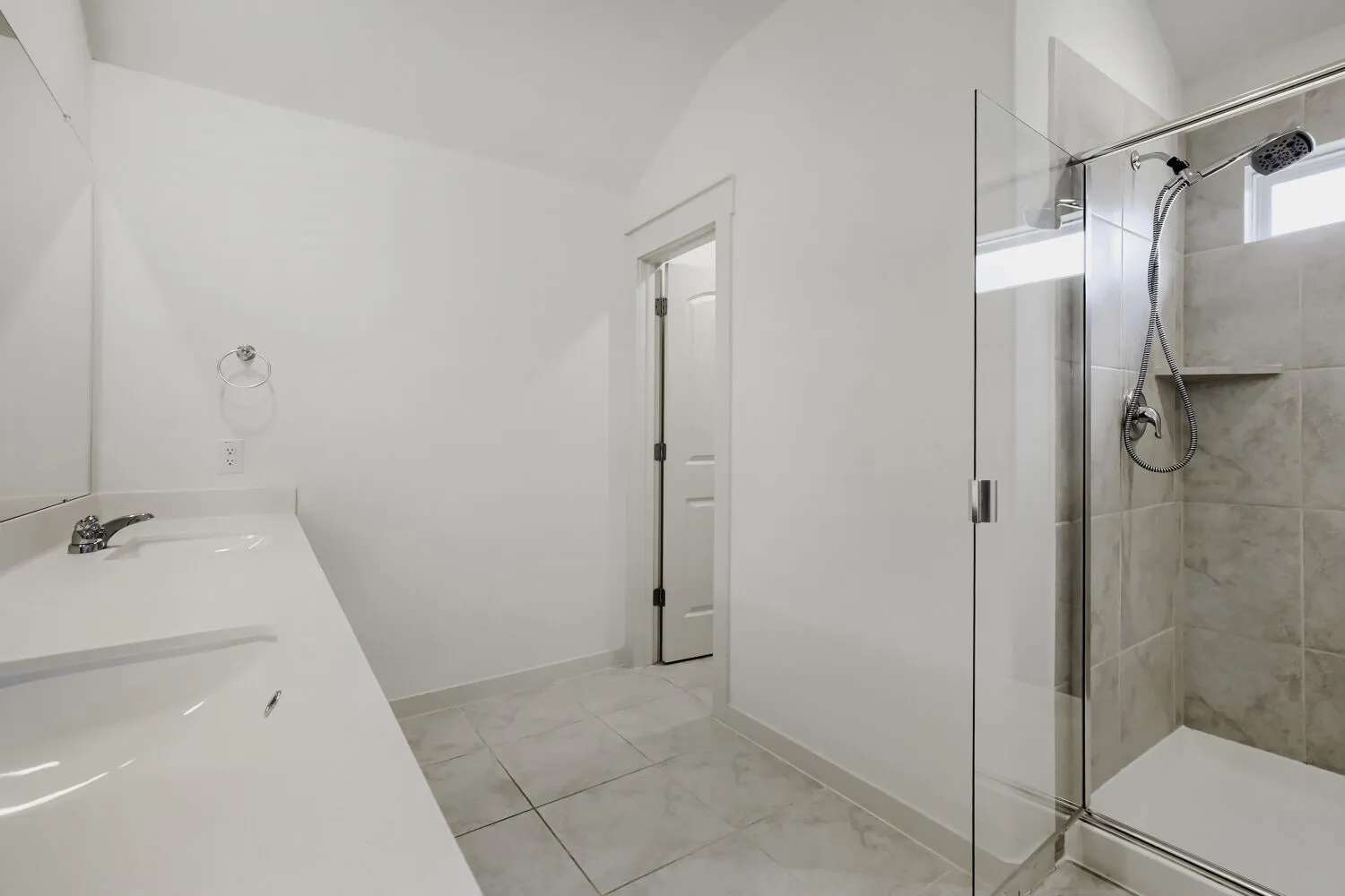 Dual vanity with integrated sinks, glass-enclosed shower, tiled shower surround with built-in niche, and tile flooring