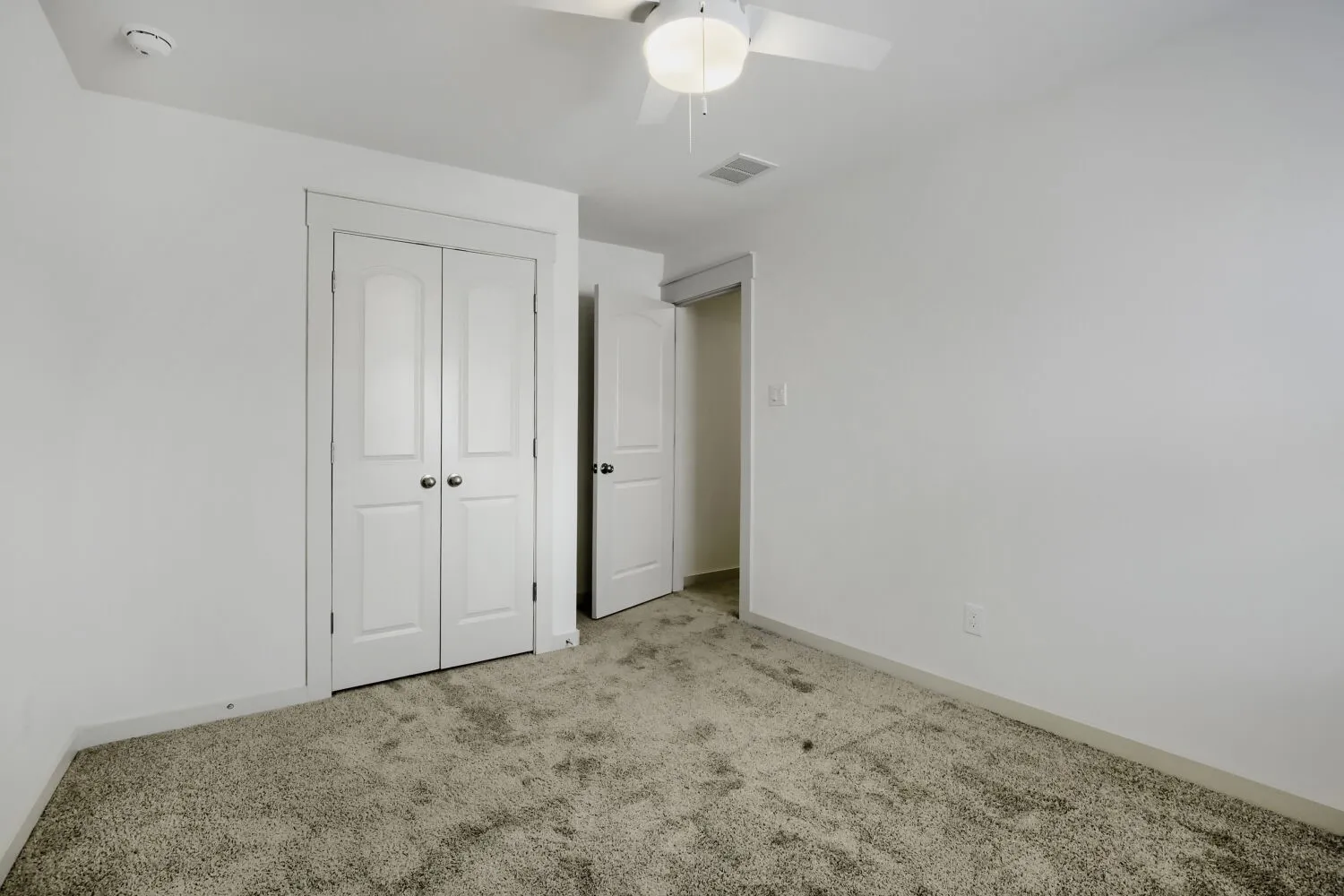 Plush carpeting, crisp white walls, and a ceiling fan with integrated lighting