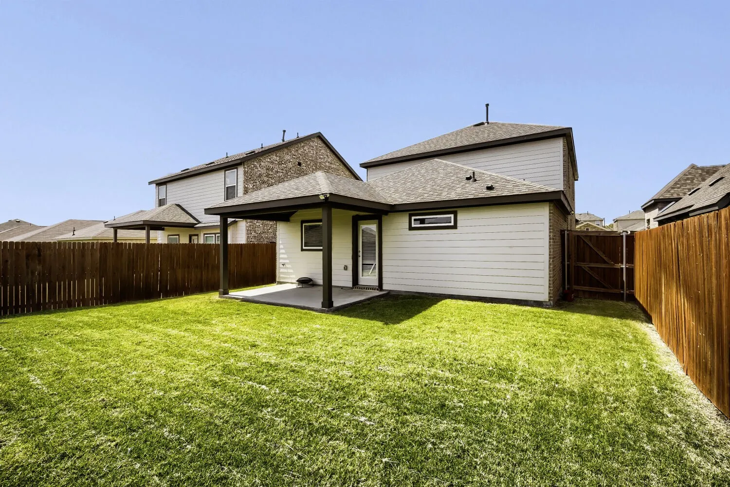 Expansive green lawn, covered patio, privacy fencing, and a side access gate
