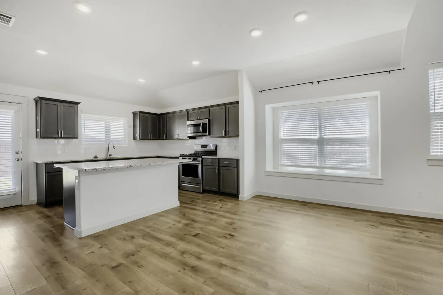 Open-concept kitchen and living area featuring wood-finish flooring, recessed lighting, a kitchen island with seating, stainless steel appliances, and white subway tile backsplash
