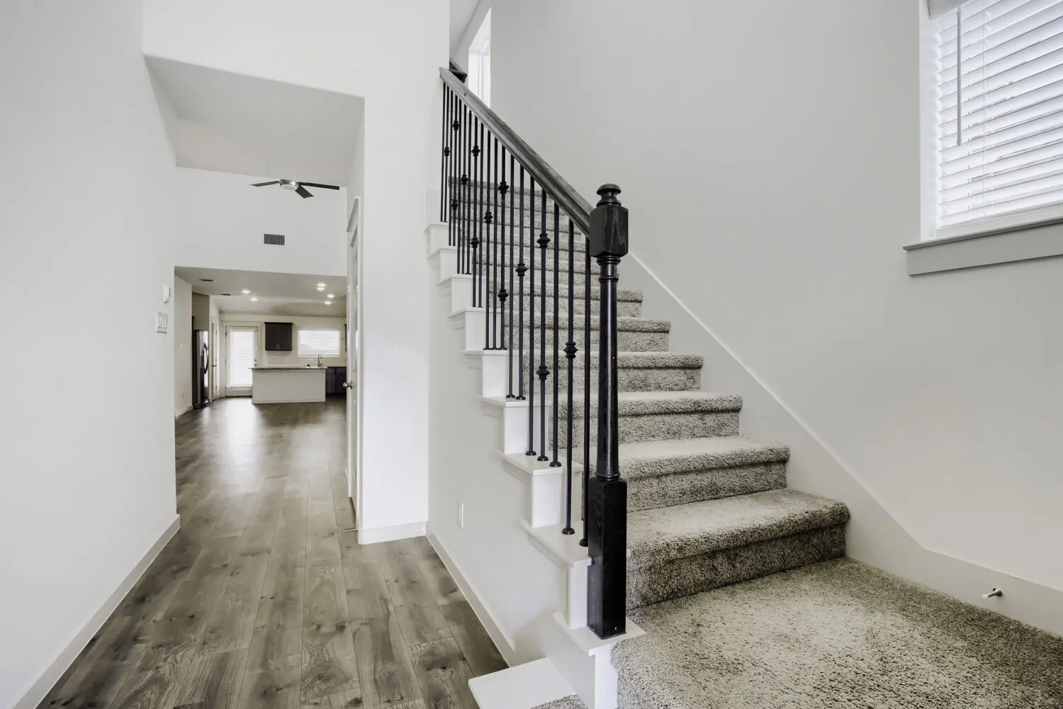 Carpeted staircase with black iron balusters, wood-finish flooring, white walls, and a ceiling fan