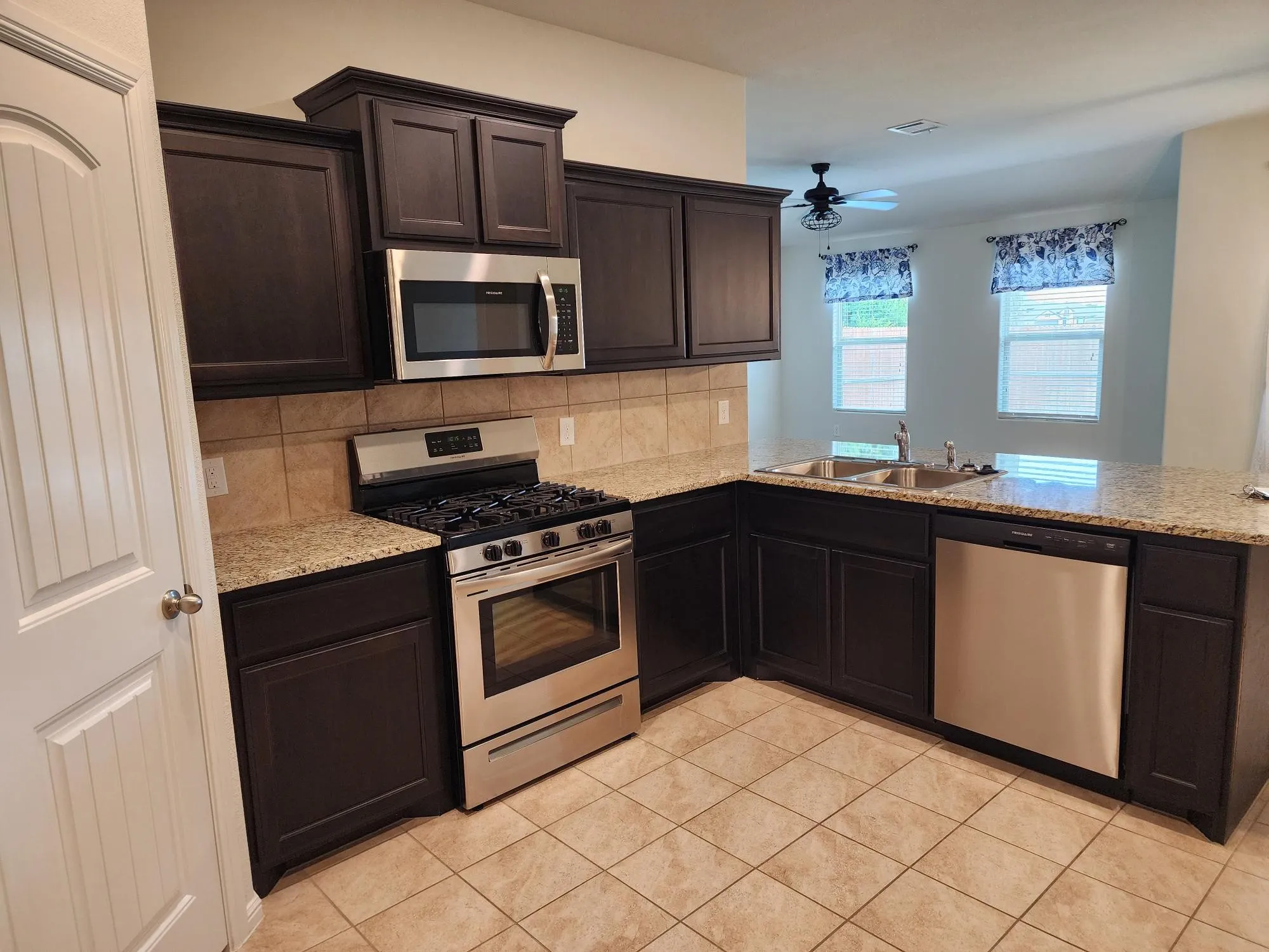 Kitchen with appliances with stainless steel finishes, backsplash, sink, ceiling fan, and light tile floors