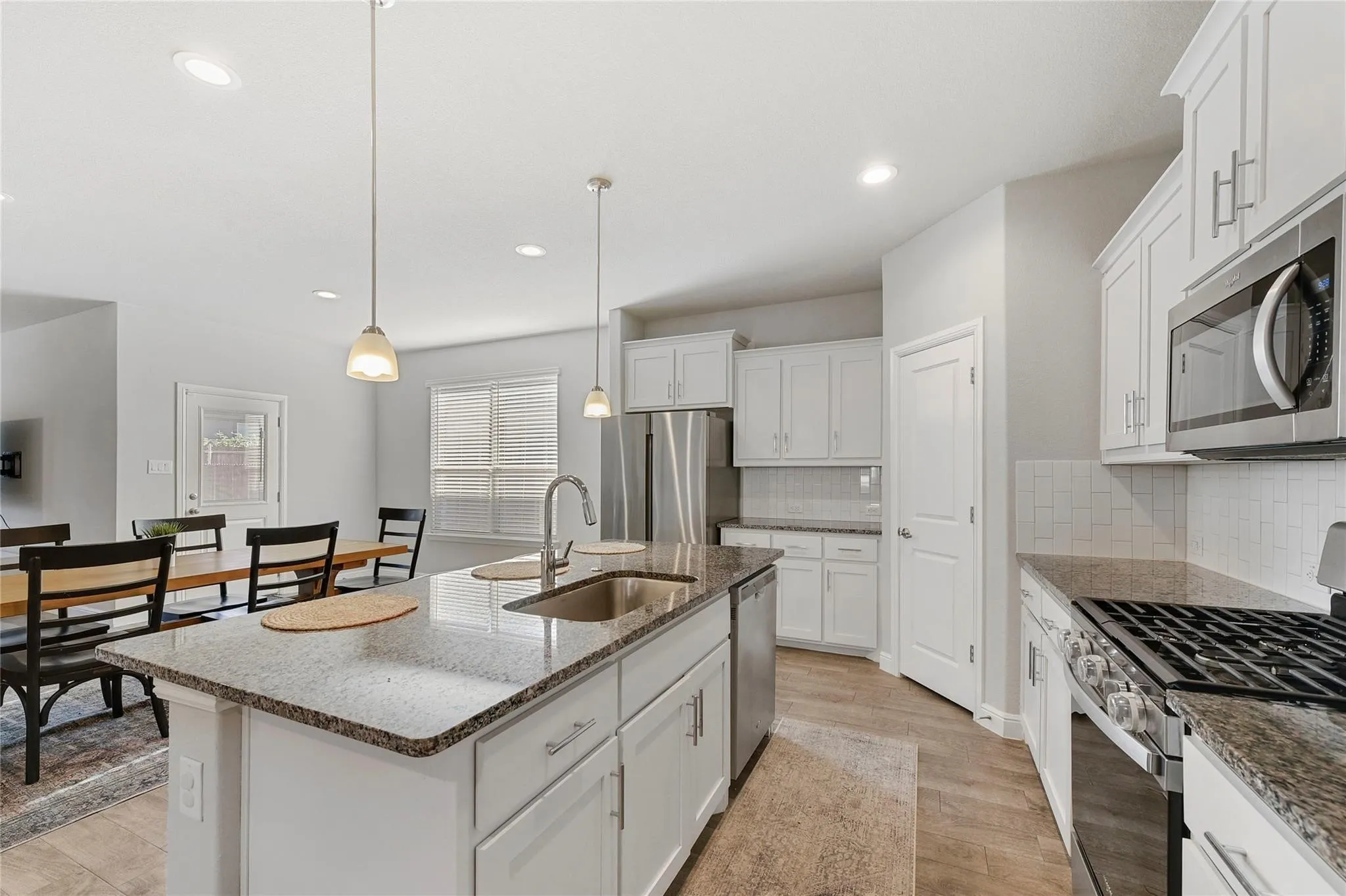 Kitchen featuring stainless steel appliances, a center island with sink, sink, pendant lighting, and light hardwood / wood-style flooring