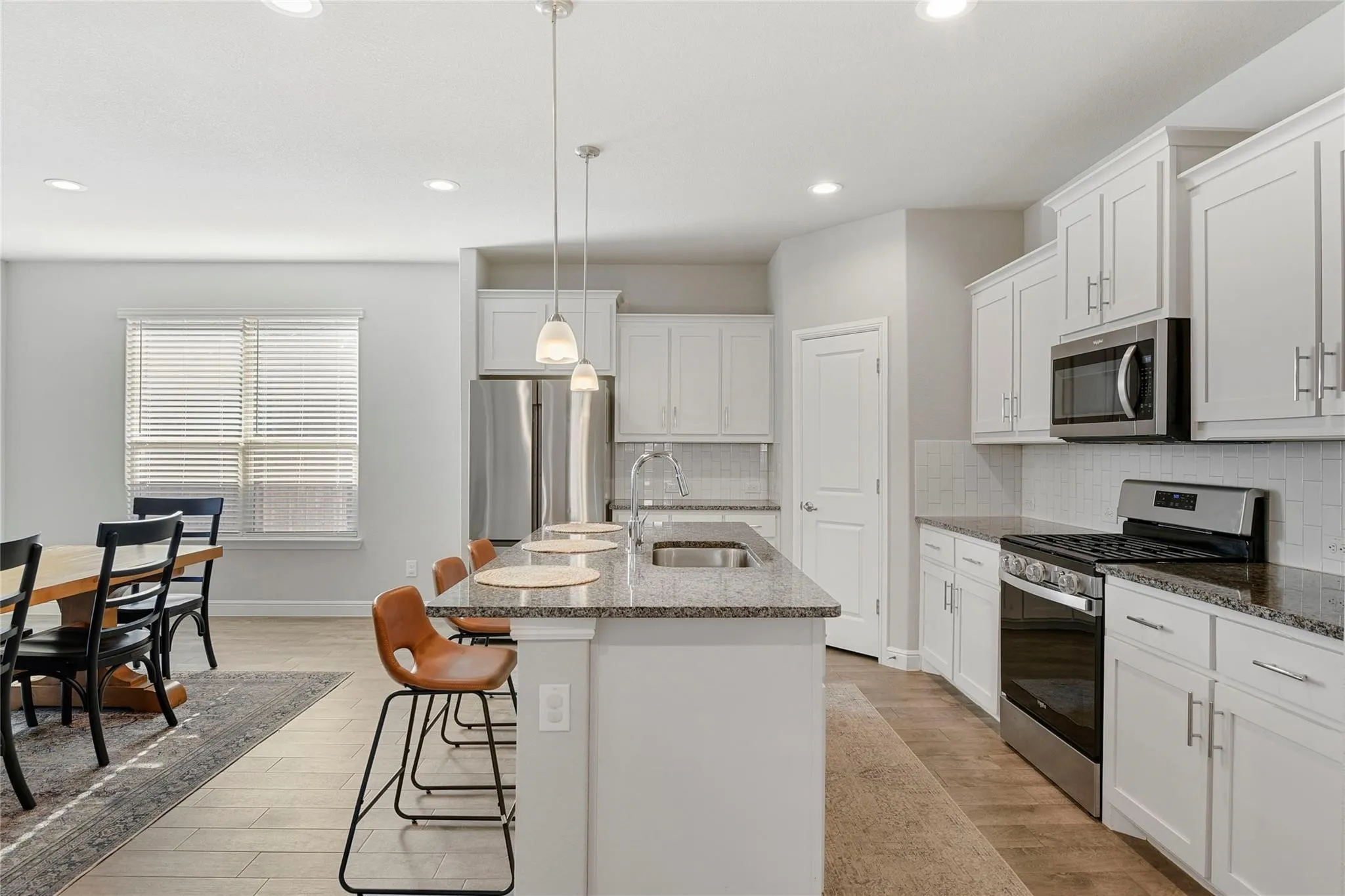 Kitchen with a center island with sink, sink, appliances with stainless steel finishes, hanging light fixtures, and white cabinets
