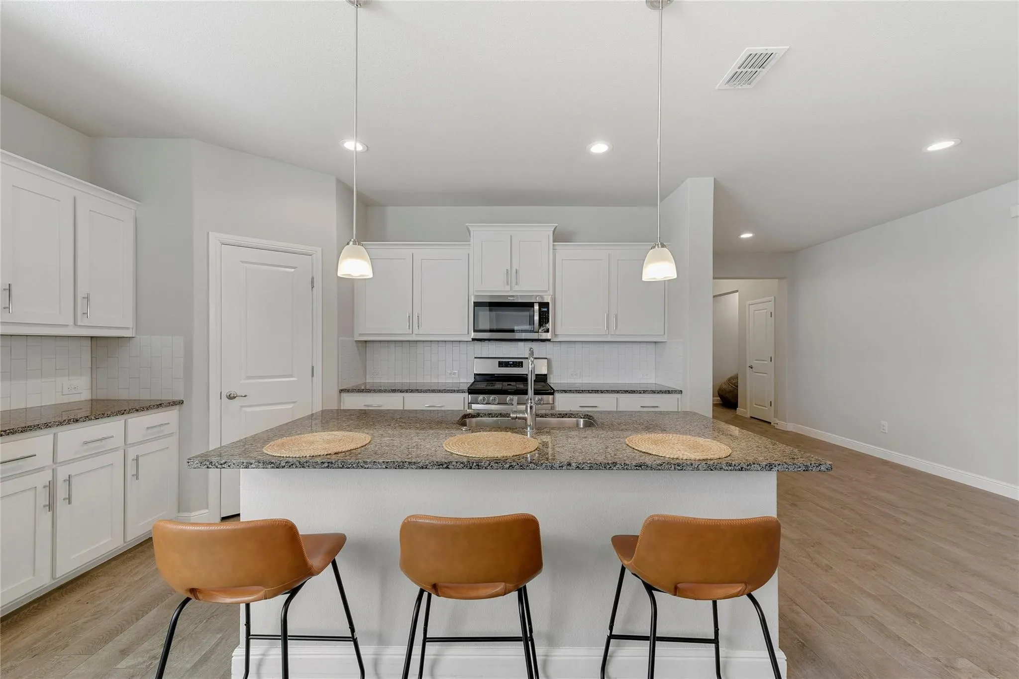 Kitchen with hanging light fixtures, an island with sink, light wood-type flooring, and appliances with stainless steel finishes