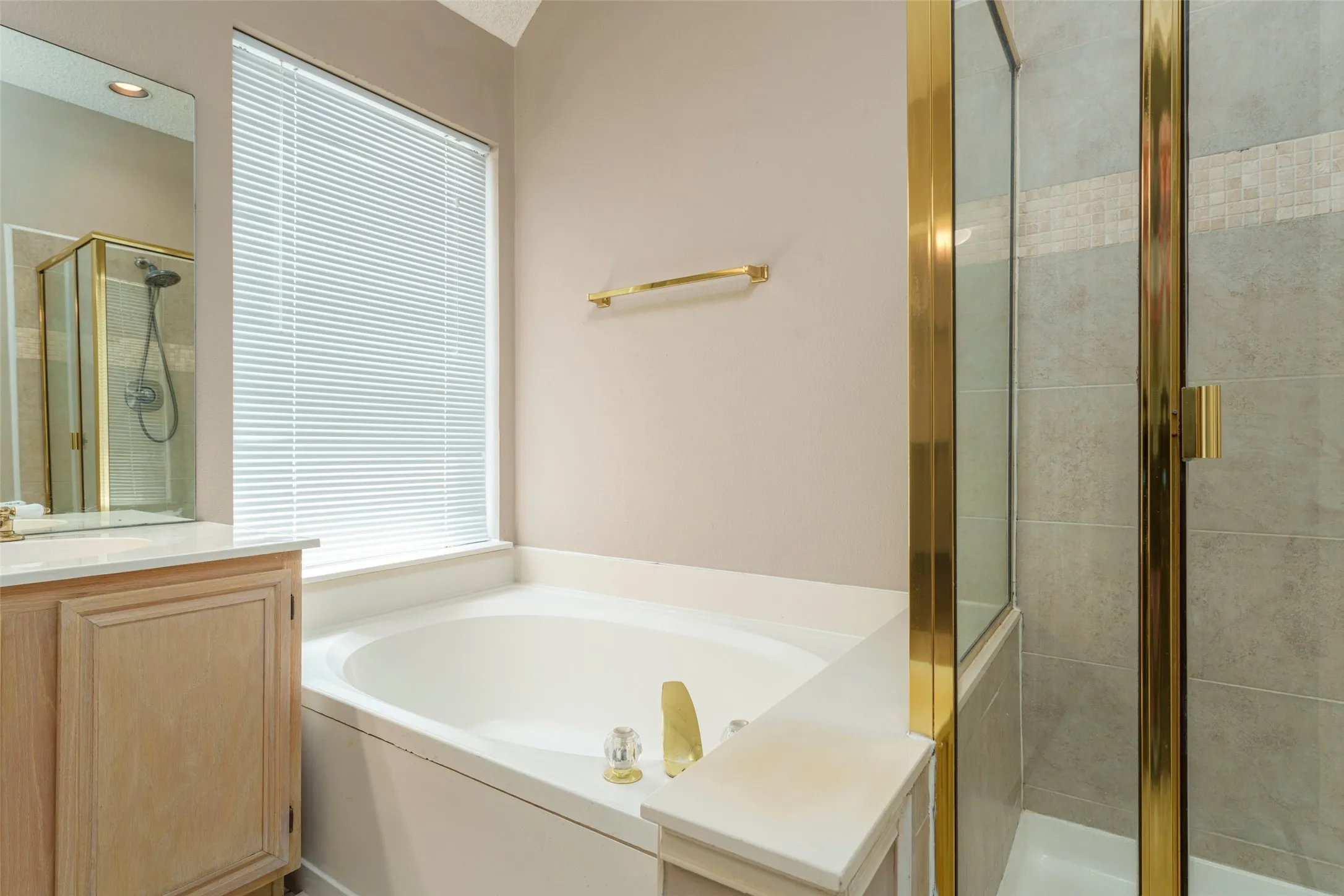 Built-in soaking tub, a separate glass-enclosed shower, light wood-finish vanity, and a large window with blinds