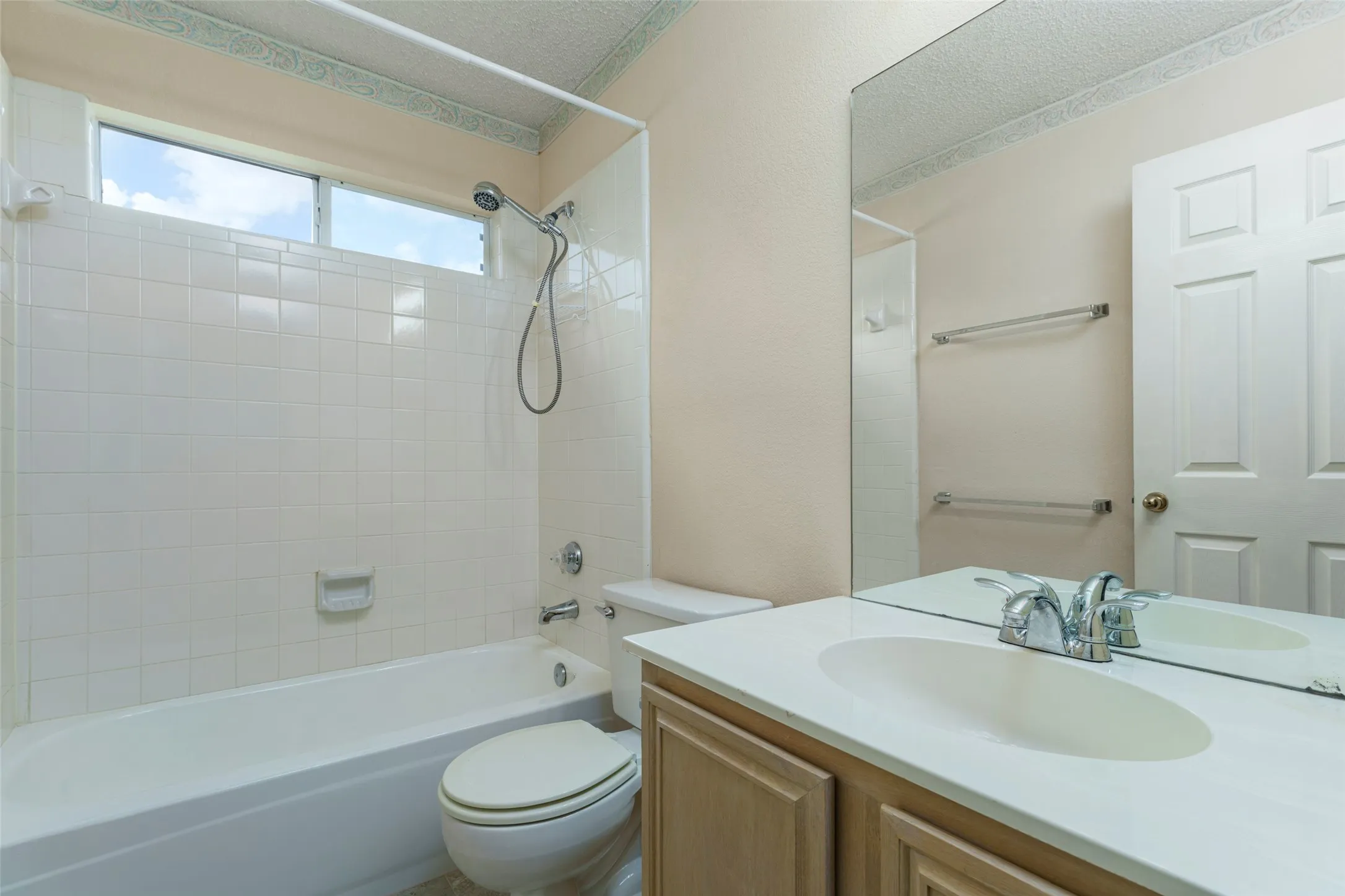 White tiled bathtub and shower combination with an overhead window, a vanity with an integrated sink, and an expansive wall mirror