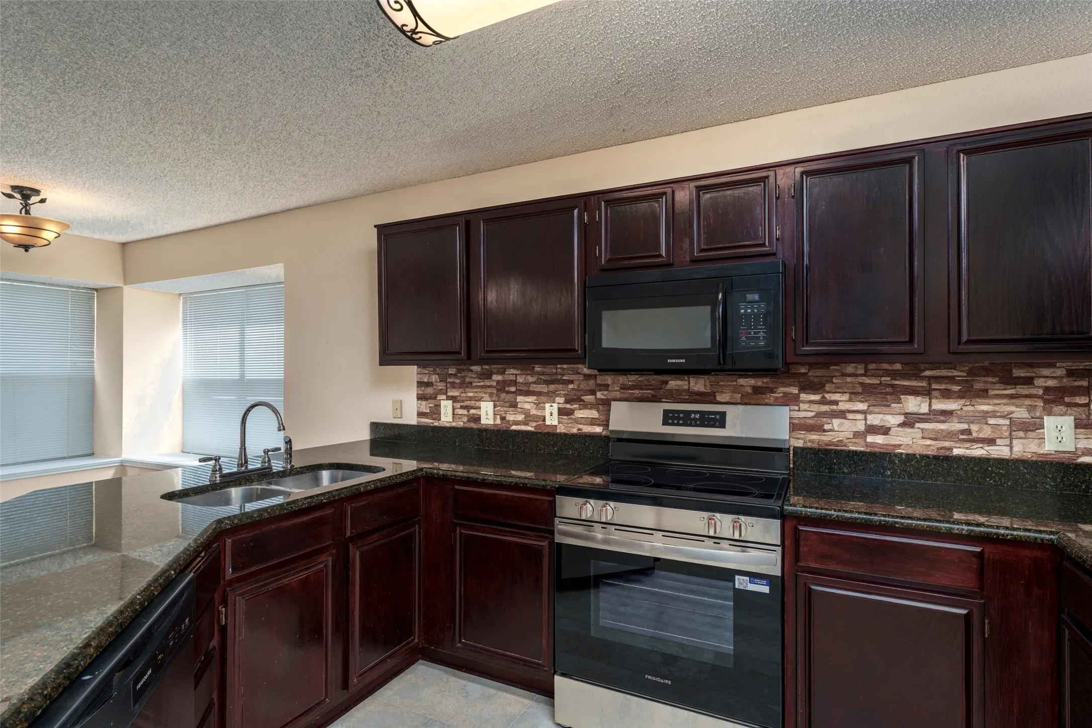 Kitchen featuring dark wood cabinetry, a mosaic tile backsplash, dark countertops, a stainless steel range, and an integrated microwave