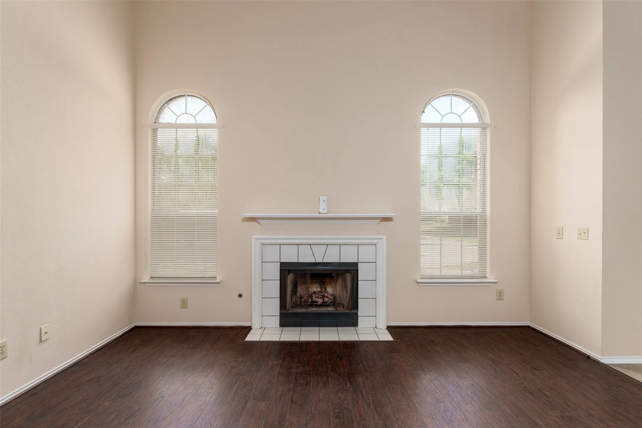 Vaulted ceiling with dual arched windows, fireplace with white tile surround, and rich wood-finish flooring