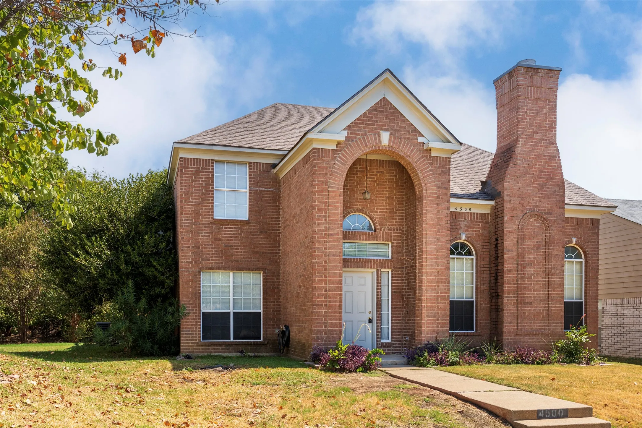 Brick exterior with an arched entry, prominent brick chimney, and a concrete pathway leading to the front door