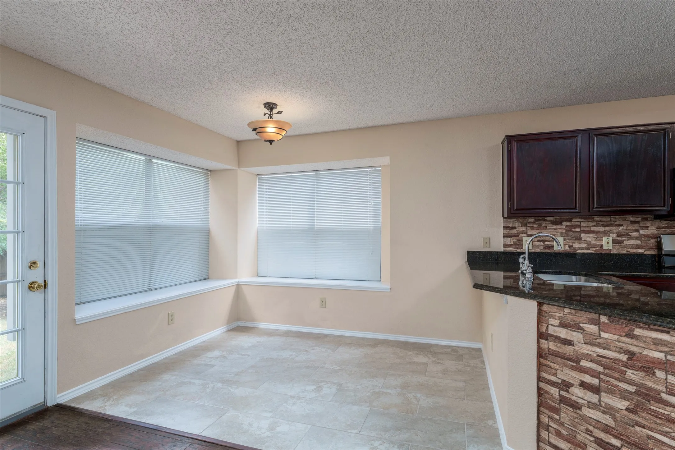 Tiled flooring, dual windows with blinds, recessed window sills, overhead light fixture, and a built-in breakfast bar with stone-finish siding