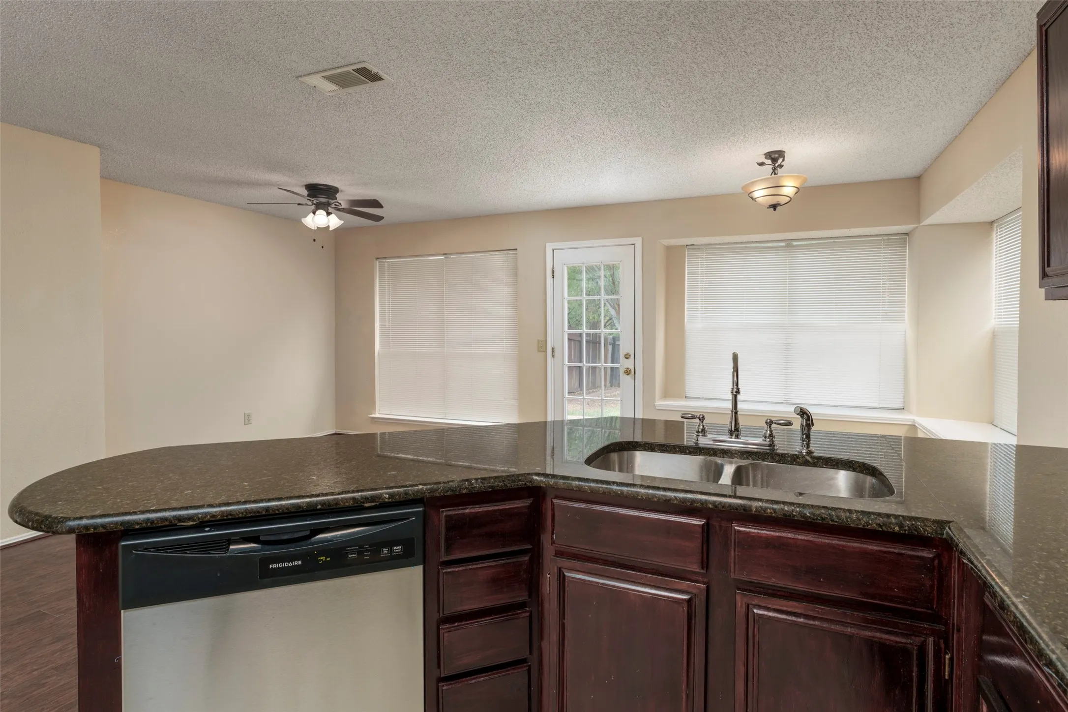 Kitchen island with a dark countertop, stainless steel dishwasher, and dark wood cabinetry