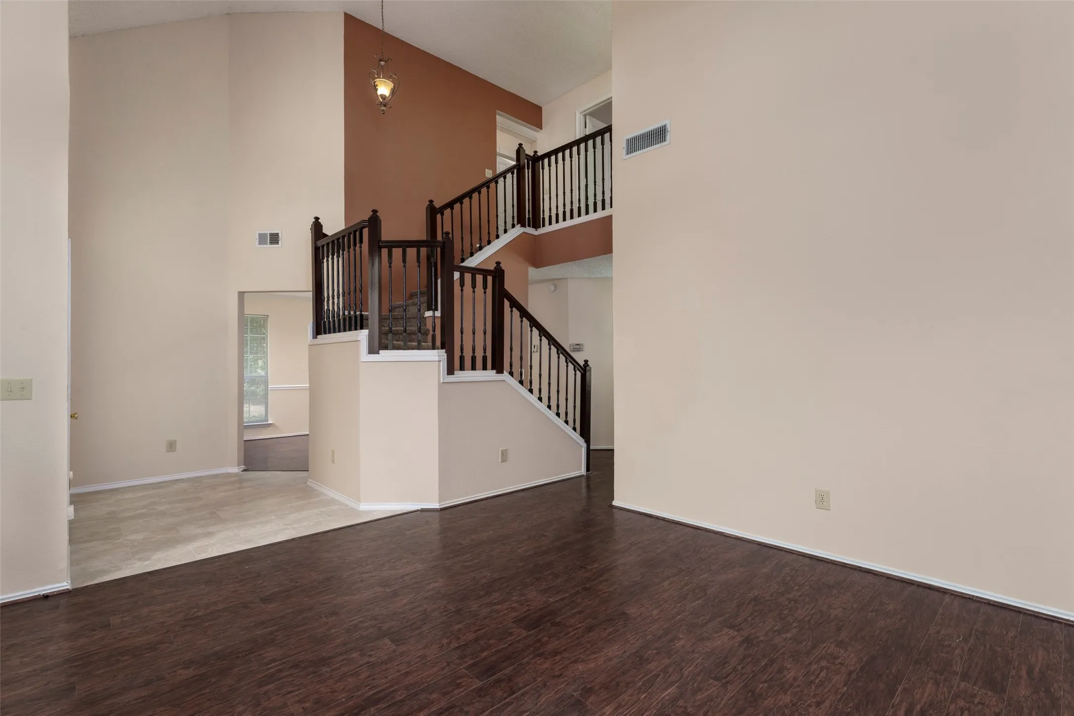 Vaulted ceiling with a hanging fixture, wood-finish flooring, and a multi-level staircase with dark wood railings