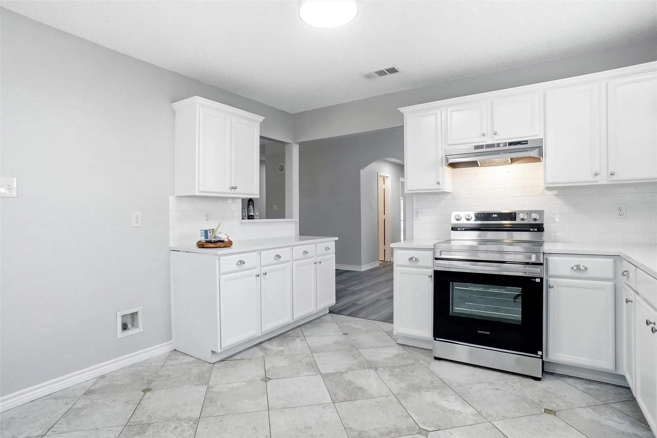 White shaker-style cabinetry, stainless steel range, light-toned tiled flooring, white subway tile backsplash, and light-toned countertops