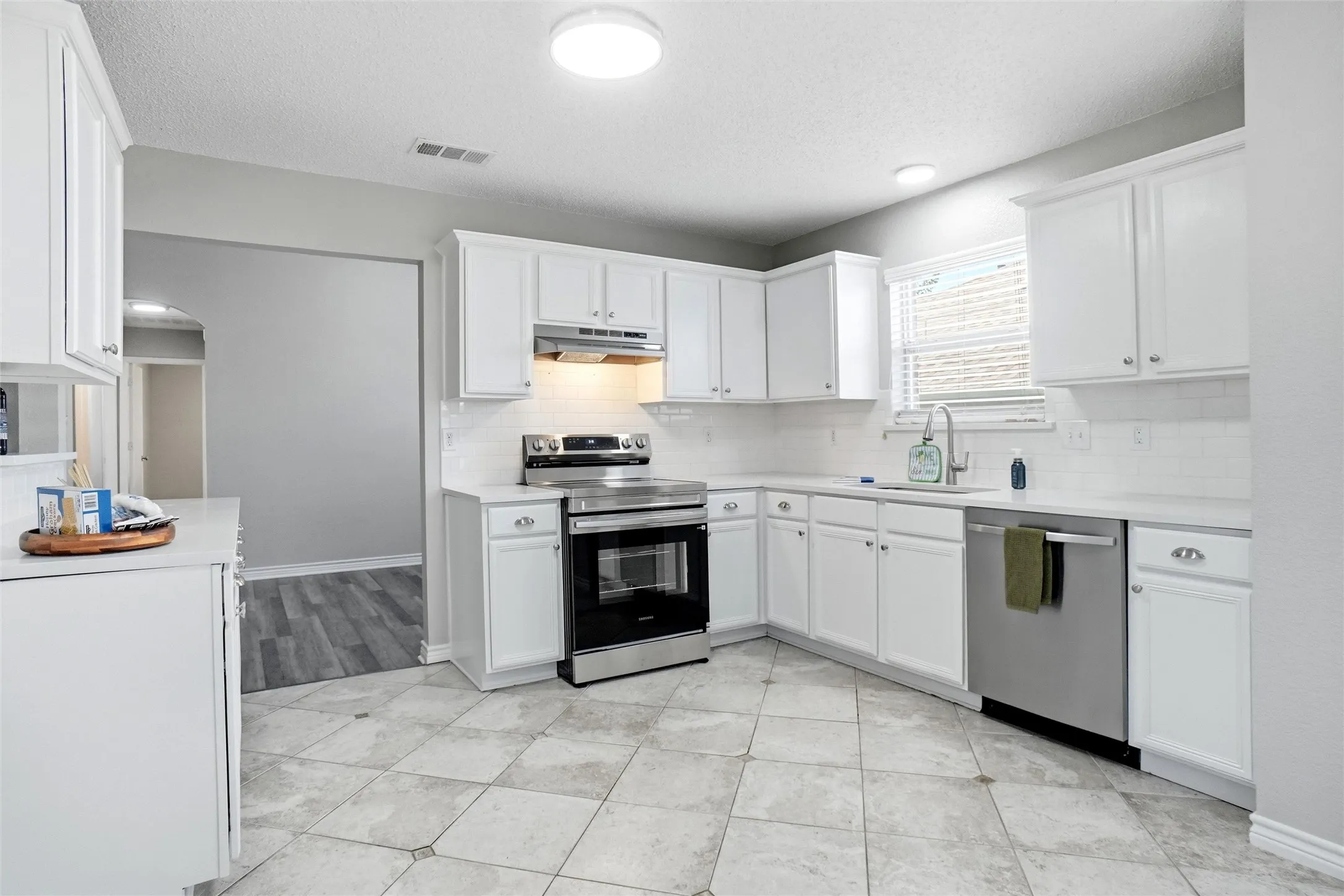 White cabinetry, stainless steel appliances, subway tile backsplash, light countertops, and tile flooring