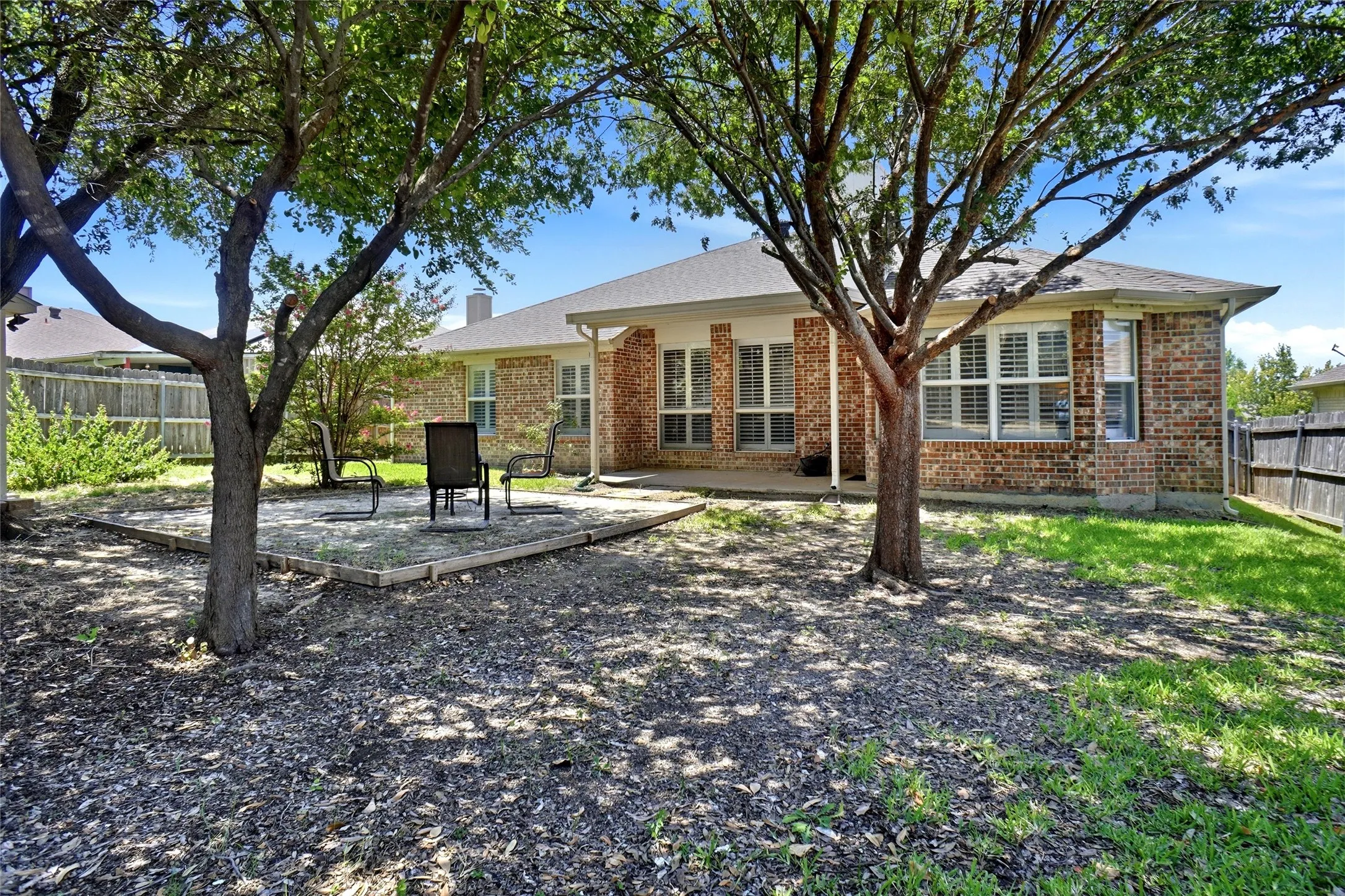 Brick exterior with multiple windows, covered patio, and a wood-fenced property line