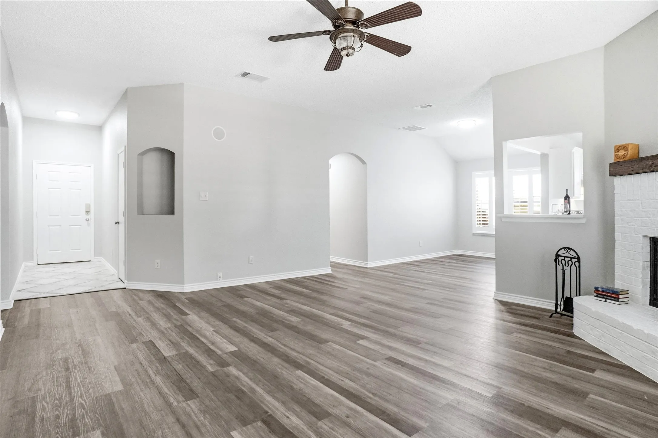 Wood-finish flooring throughout, vaulted ceilings, arched doorways, a built-in niche, and a whitewashed brick fireplace