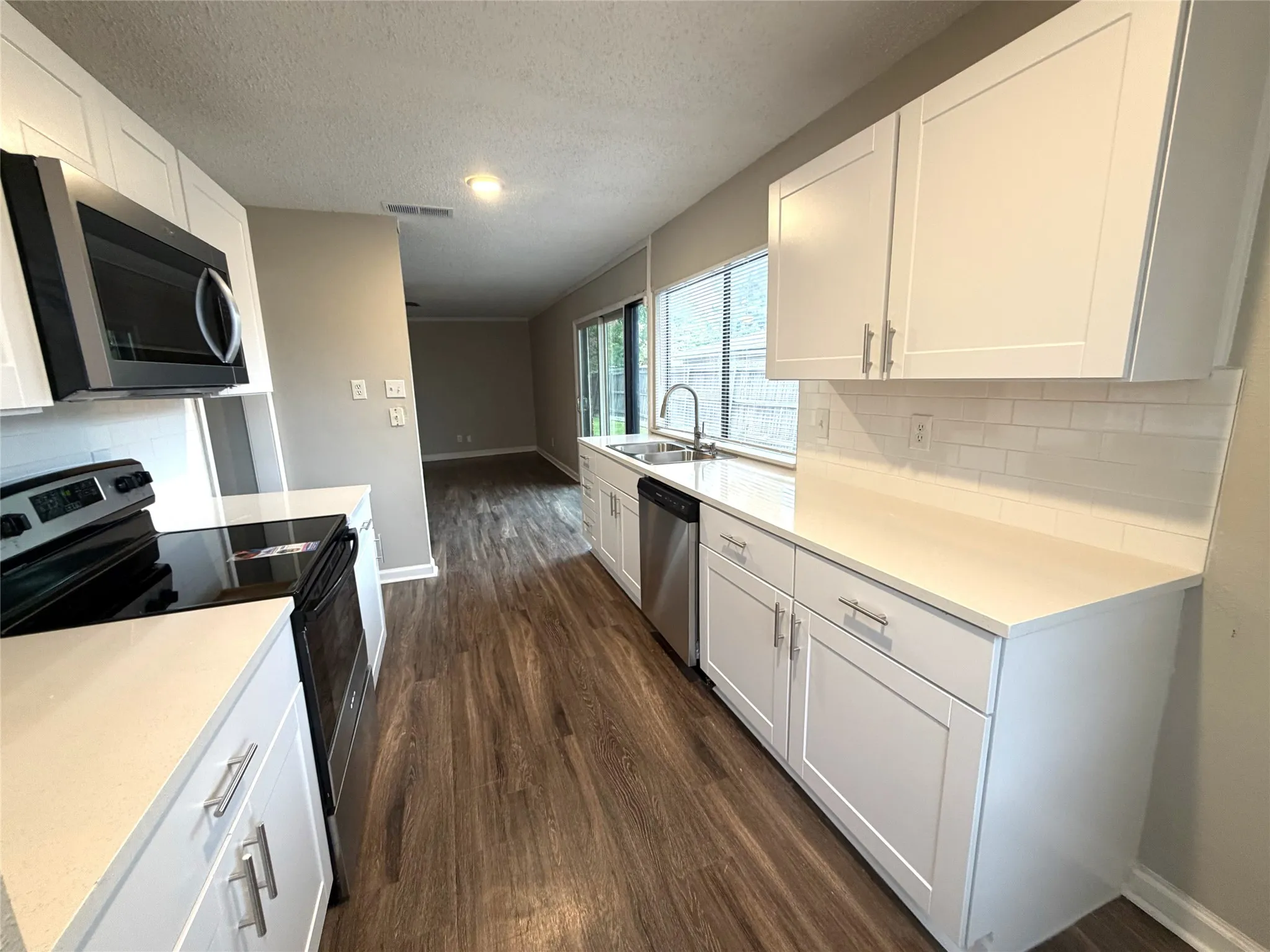 Contemporary kitchen featuring white cabinetry, light countertops, wood-finish flooring, and stainless steel appliances