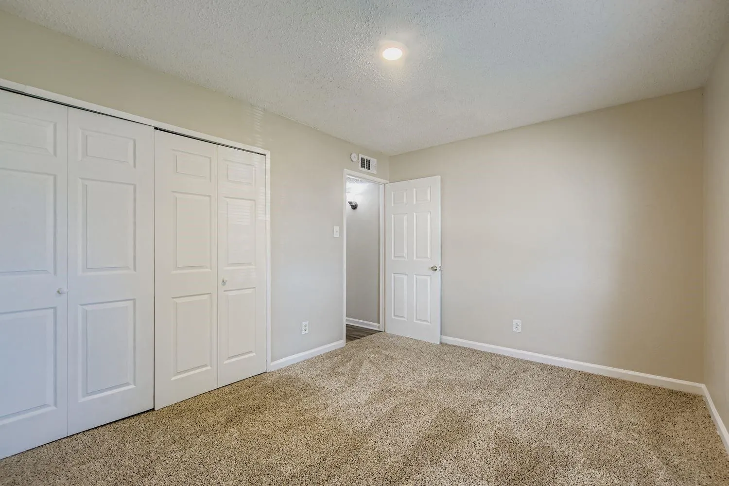 Neutral wall color, carpet flooring, a single overhead light fixture, and two sets of bi-fold closet doors