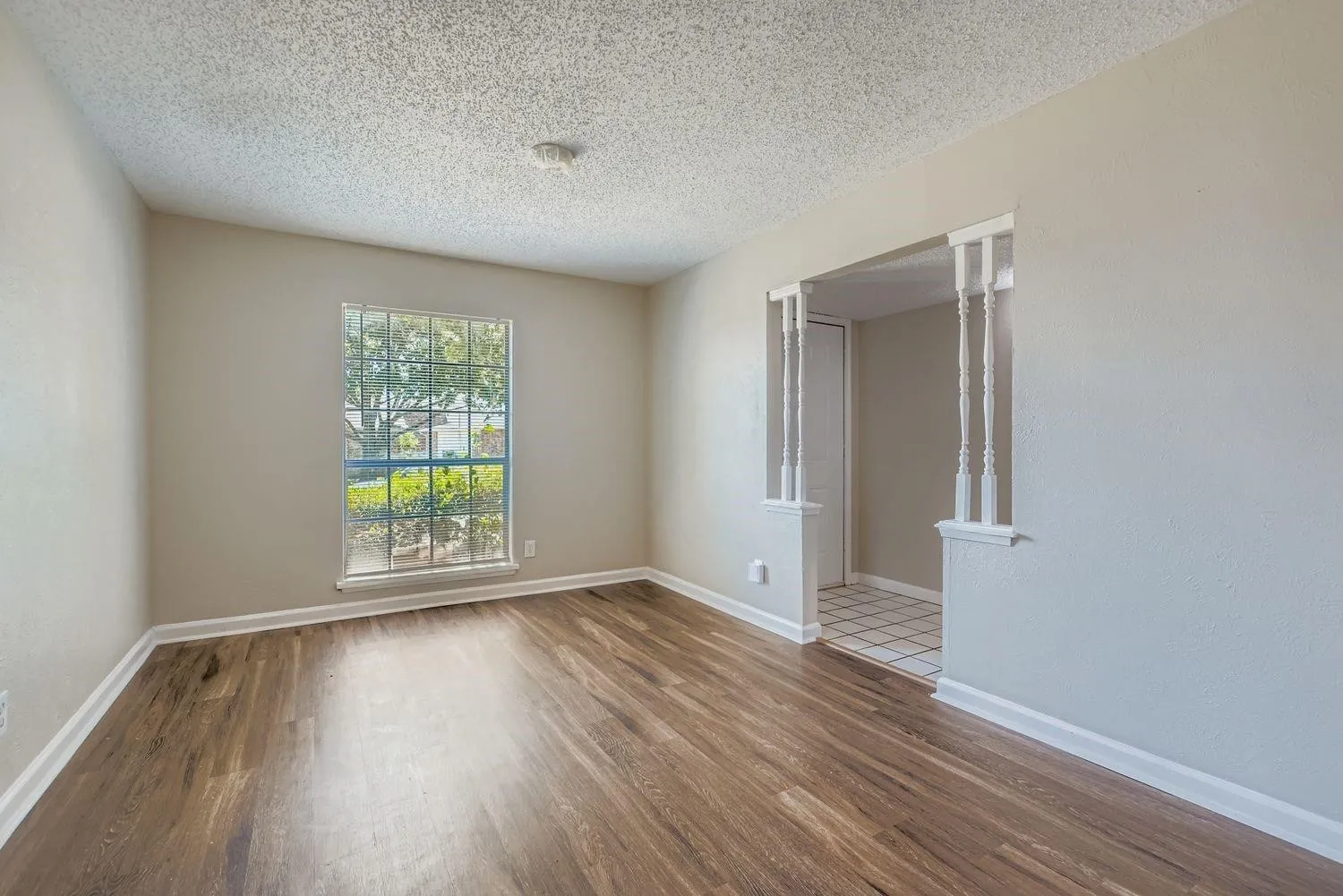 Wood-finish flooring, neutral wall paint, a window with exterior landscaping, and an arched entryway featuring decorative pillars