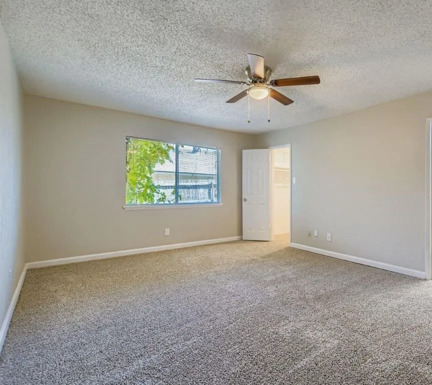 Carpeted flooring, neutral wall tones, window, ceiling fan with integrated lighting, and a closet with shelving