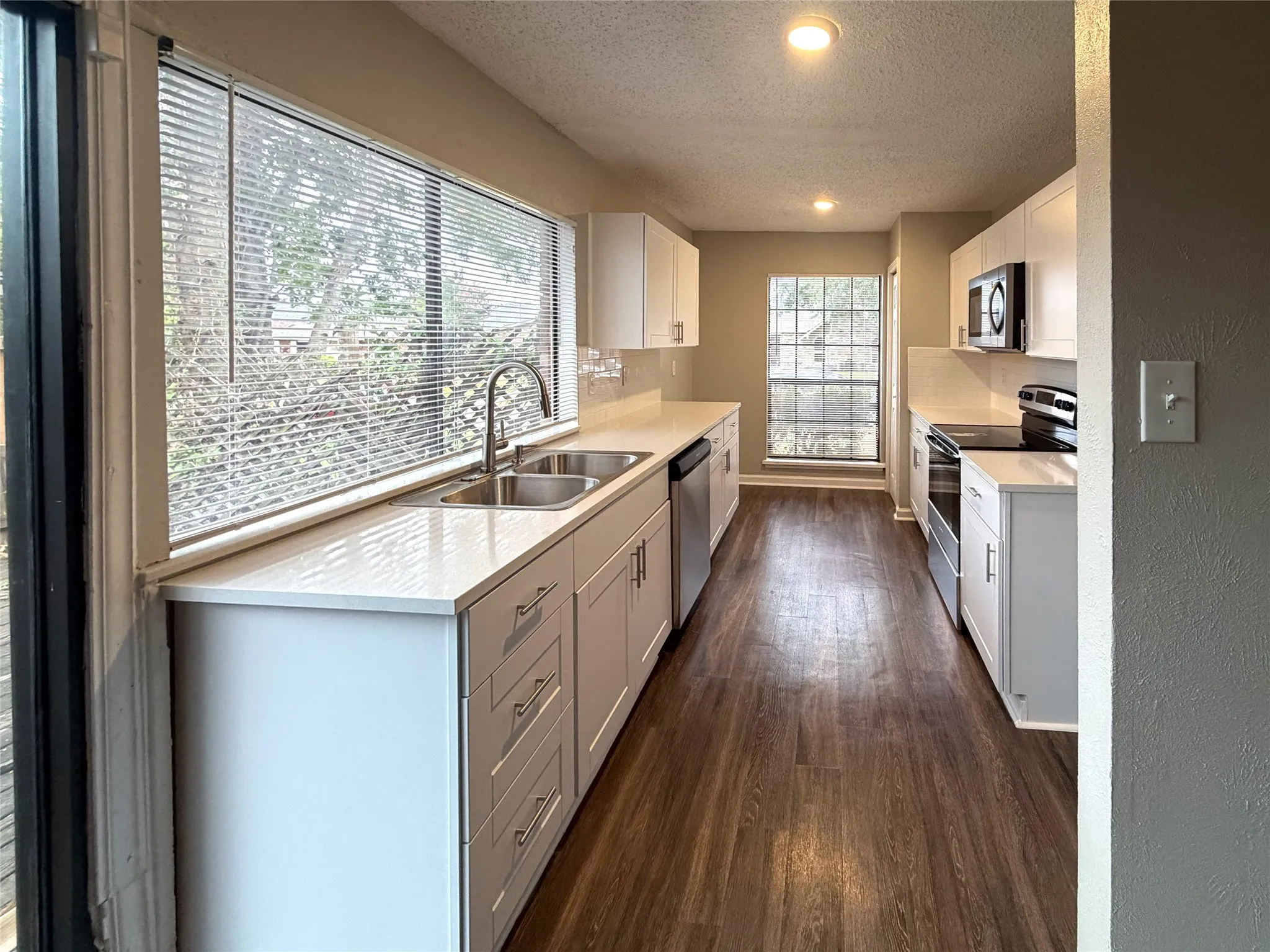 Contemporary kitchen with white cabinetry, stainless steel sink, sleek countertops, and wood-finish flooring