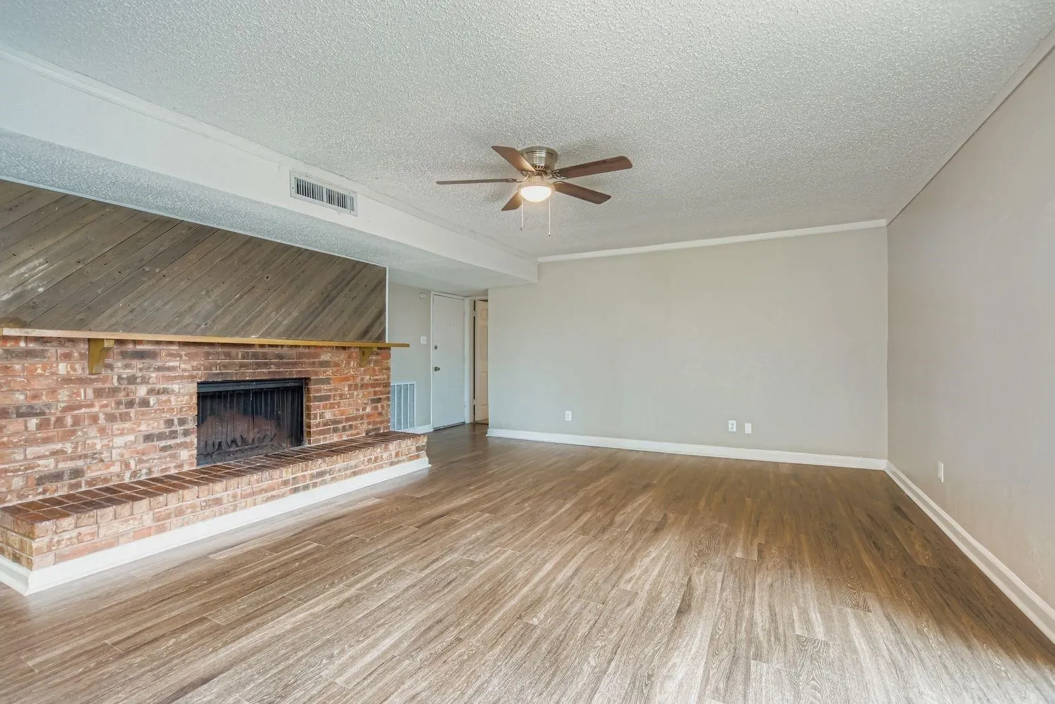 Spacious room with wood-finish flooring, a brick fireplace with wood mantel, and a ceiling fan