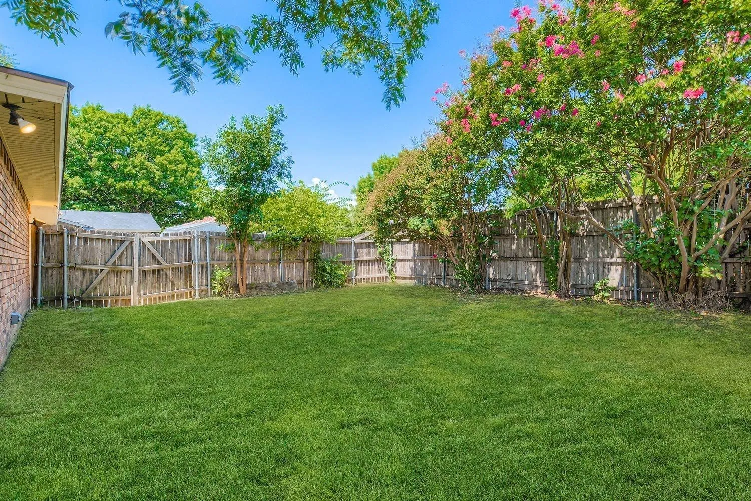 Expansive backyard featuring a manicured lawn, wood privacy fencing, and mature trees with pink floral accents